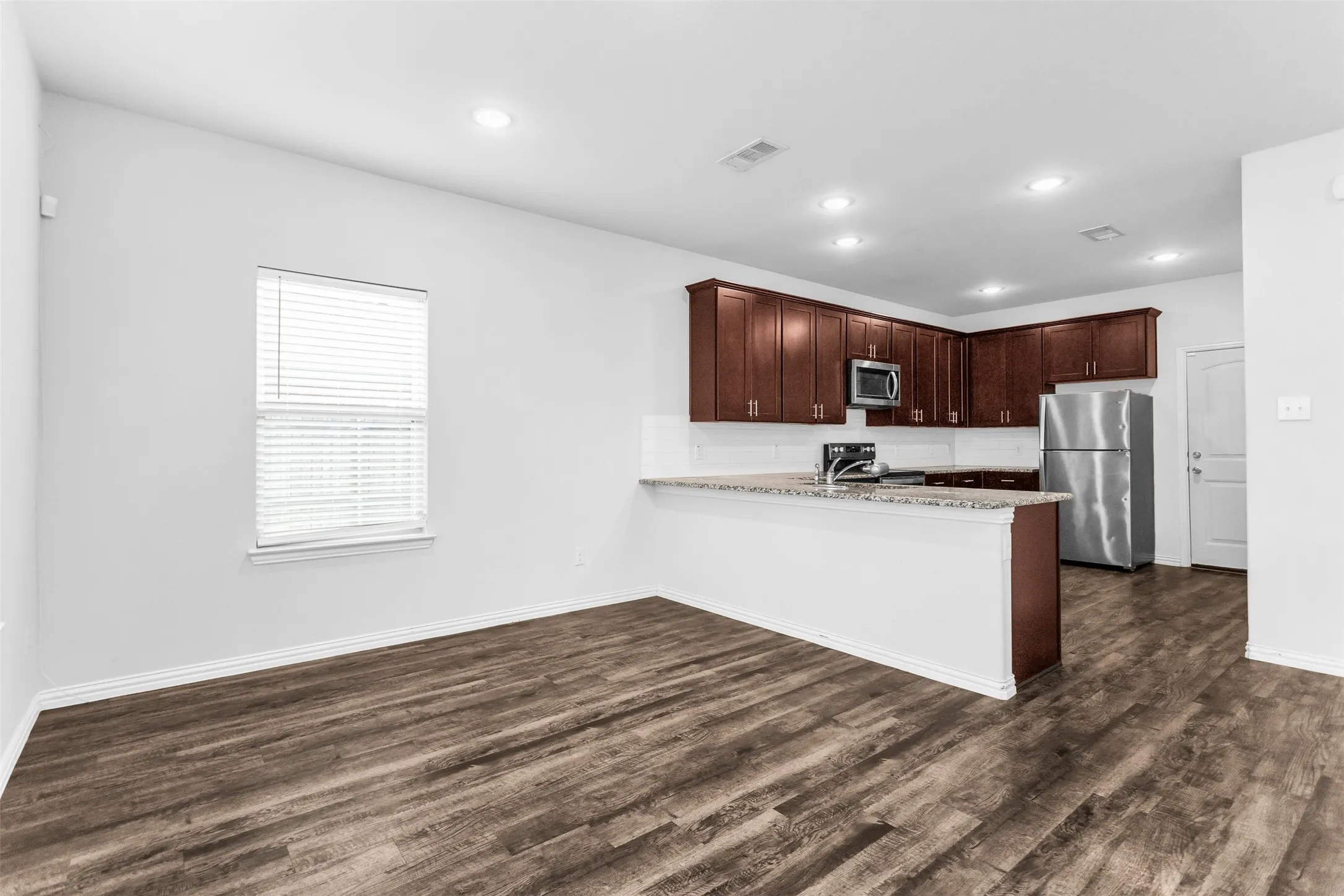 Wood-finish flooring throughout, recessed lighting, and a kitchen featuring dark wood cabinetry, light-toned countertops, and stainless steel appliances