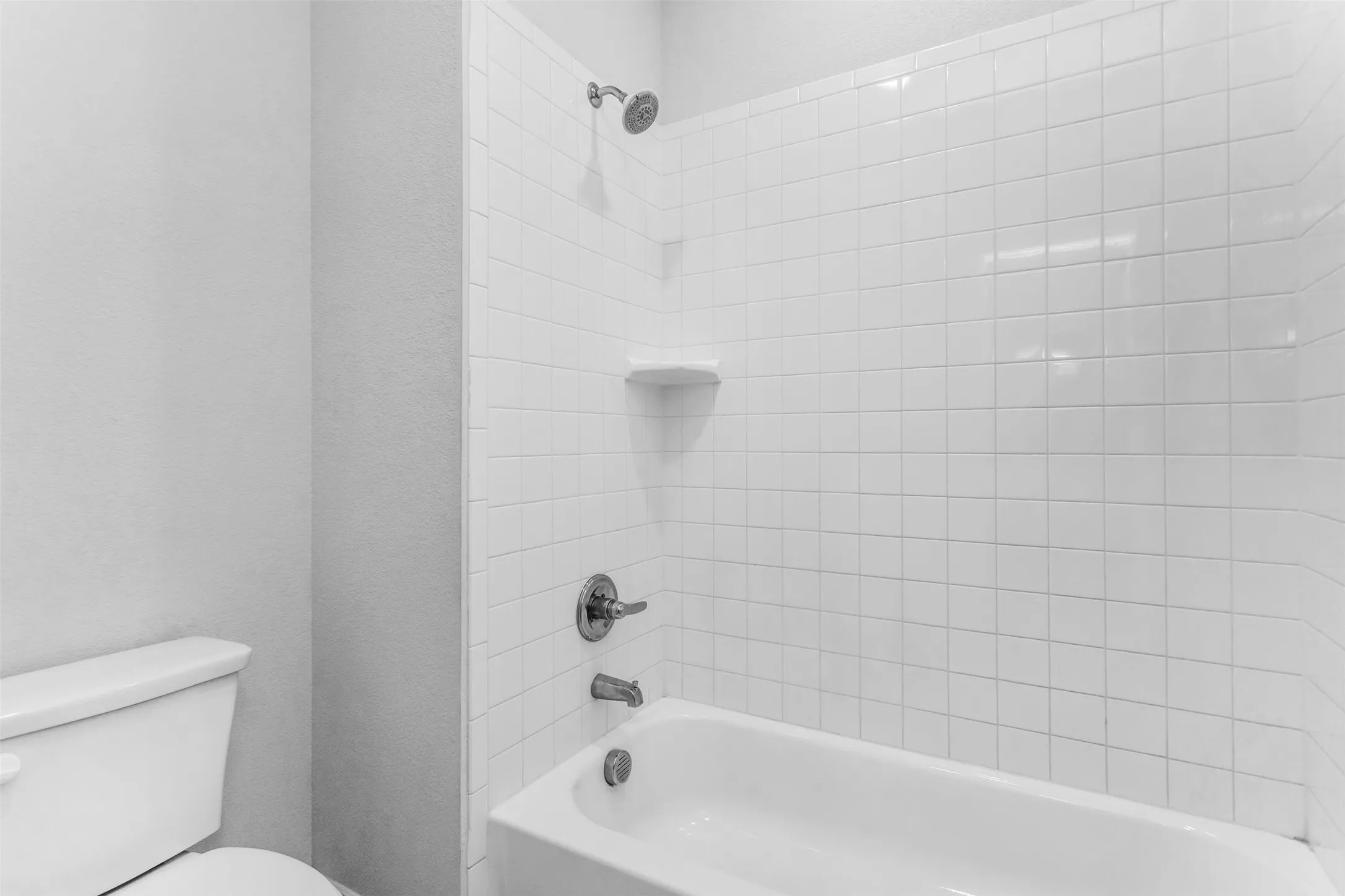 White subway tile tub surround with integrated shelf, polished chrome shower head, and matching fixtures