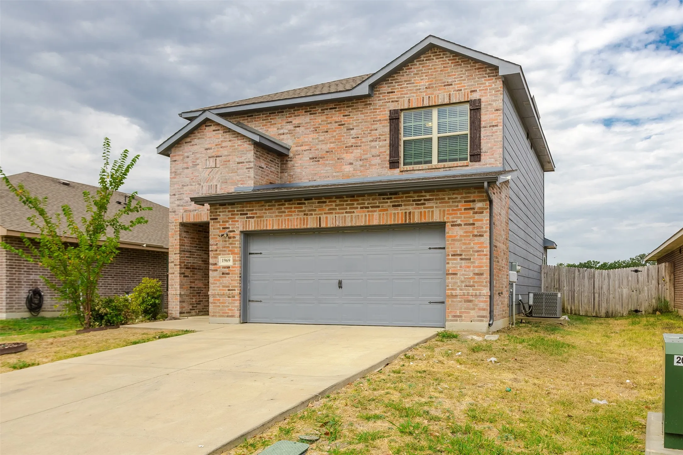 Brick exterior with gray siding accents, attached garage, concrete driveway, and covered entry