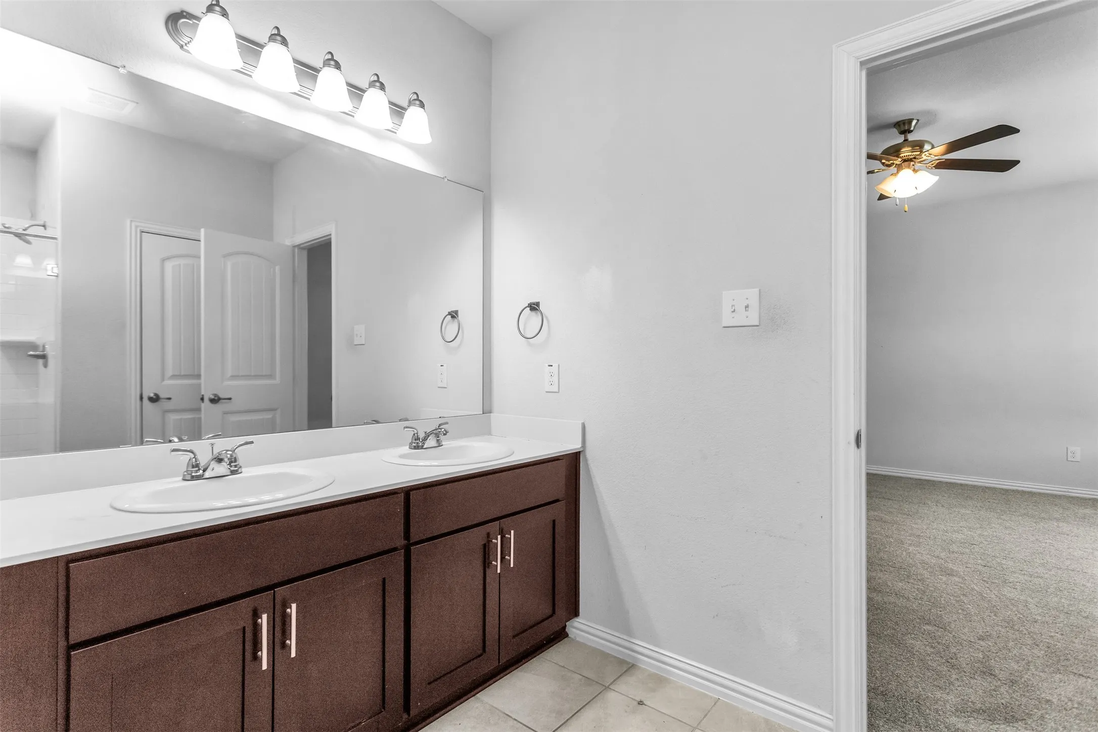 Dual vanity with white undermount sinks, wall-mounted lighting, and dark wood-finish cabinetry