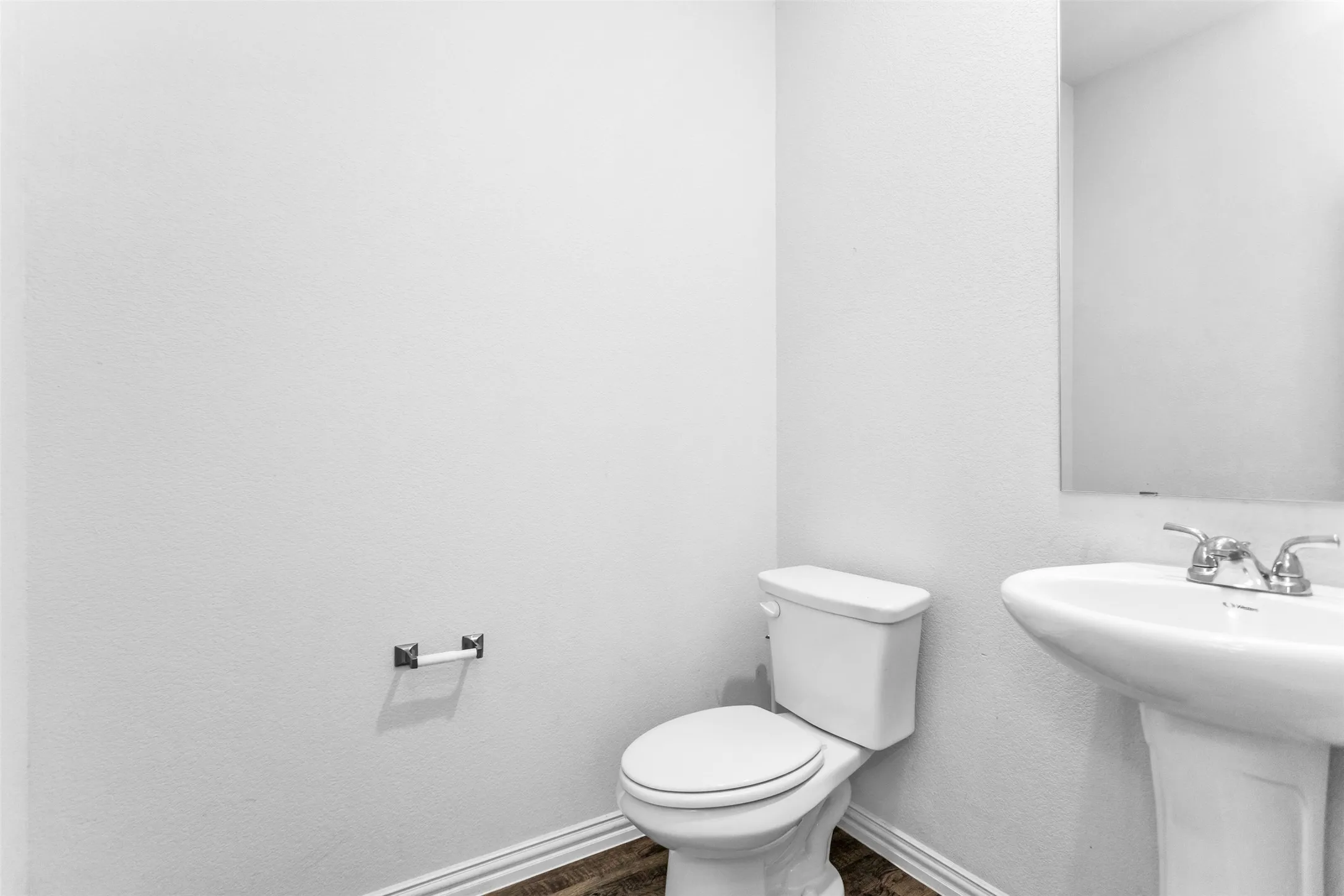 Pedestal sink with chrome faucet, wall-mounted mirror, and wood-finish flooring