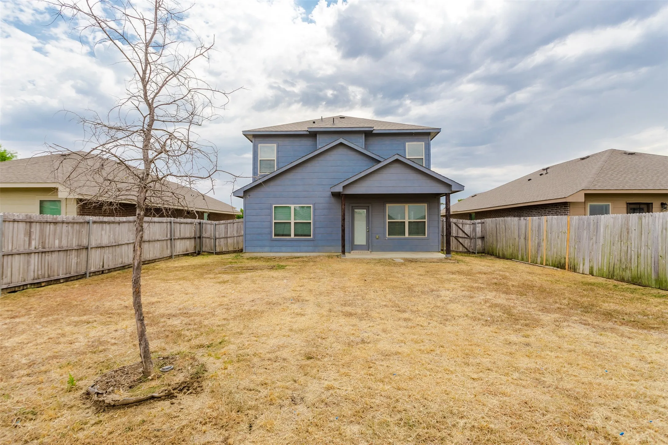 Two-story residence with blue siding, a covered patio, and a fenced perimeter