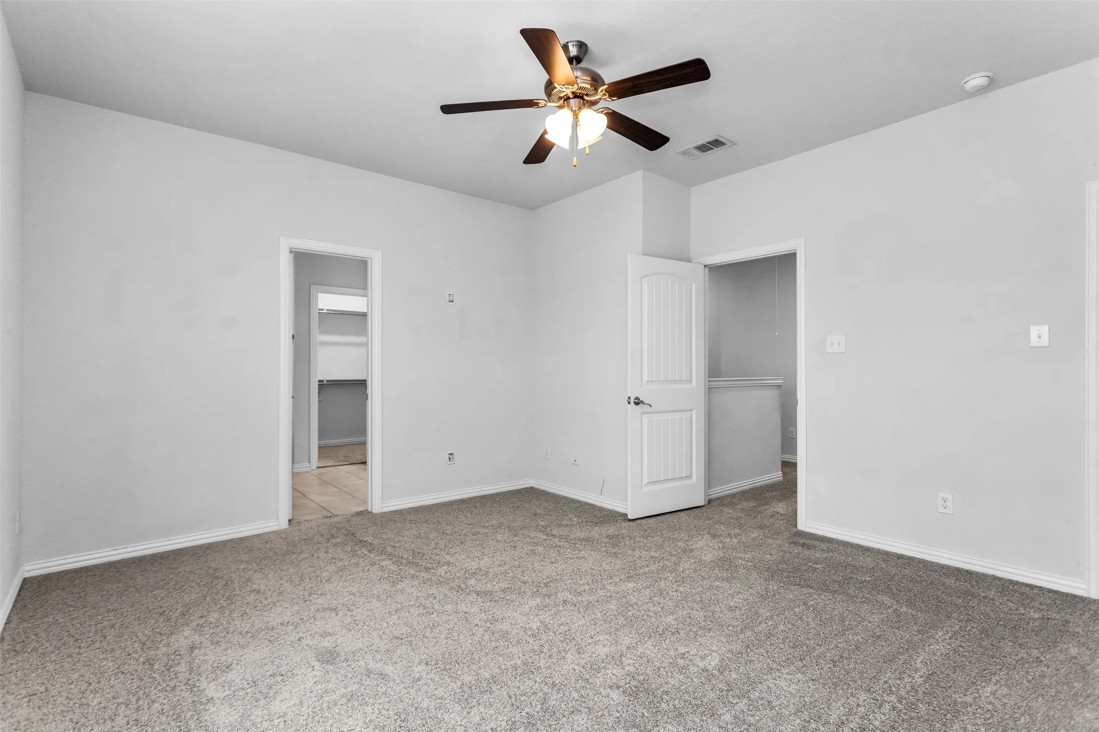 Spacious room featuring neutral carpet, light gray walls, a ceiling fan with integrated lighting, and white paneled doors