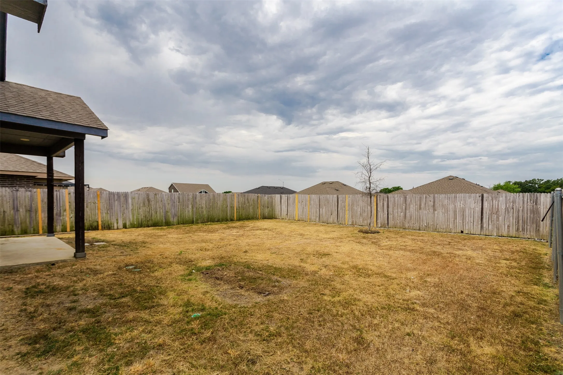 Backyard with a wood privacy fence, concrete patio, and a covered patio area with dark support posts