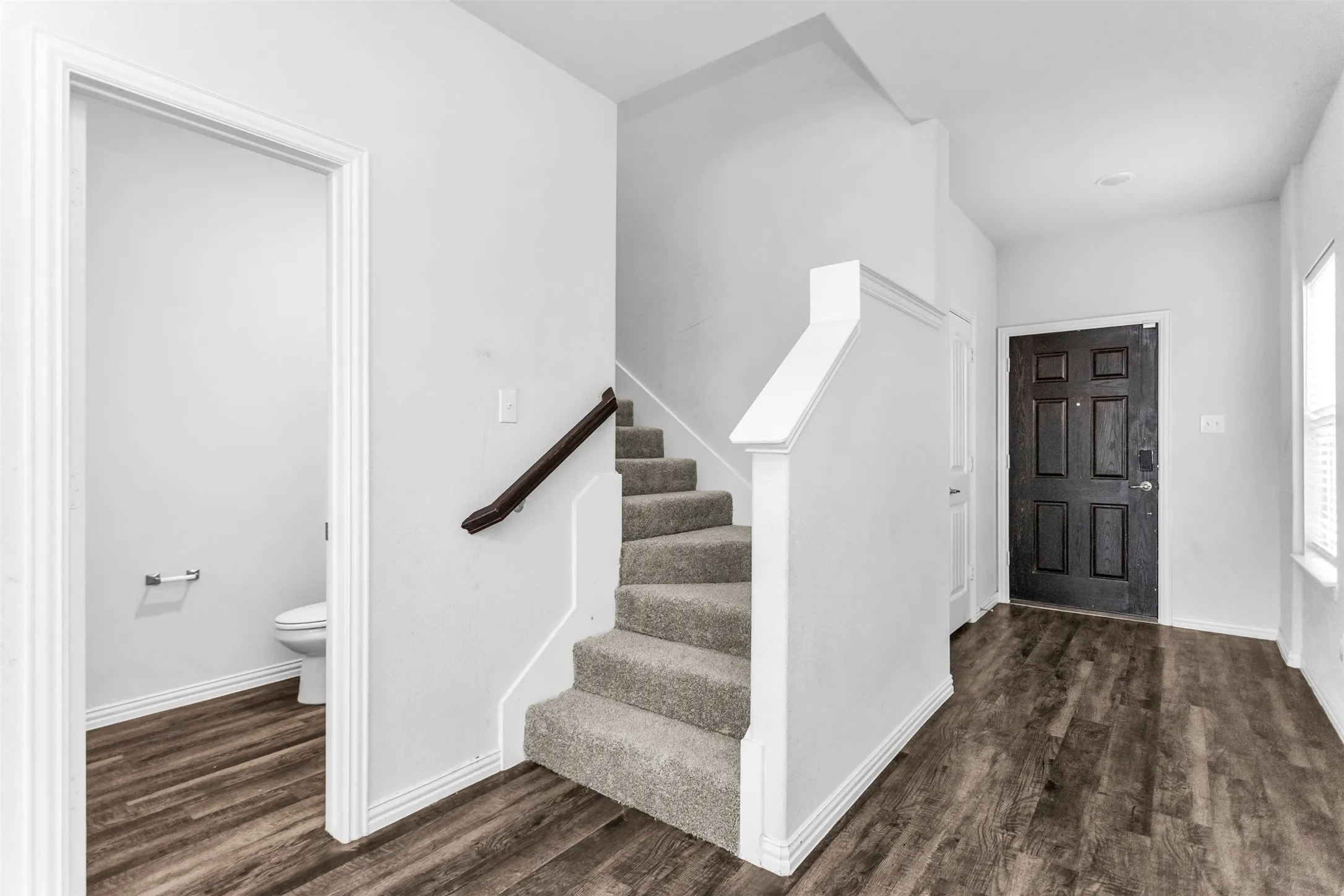 Wood-finish flooring throughout the entry, carpeted staircase, and paneled front door