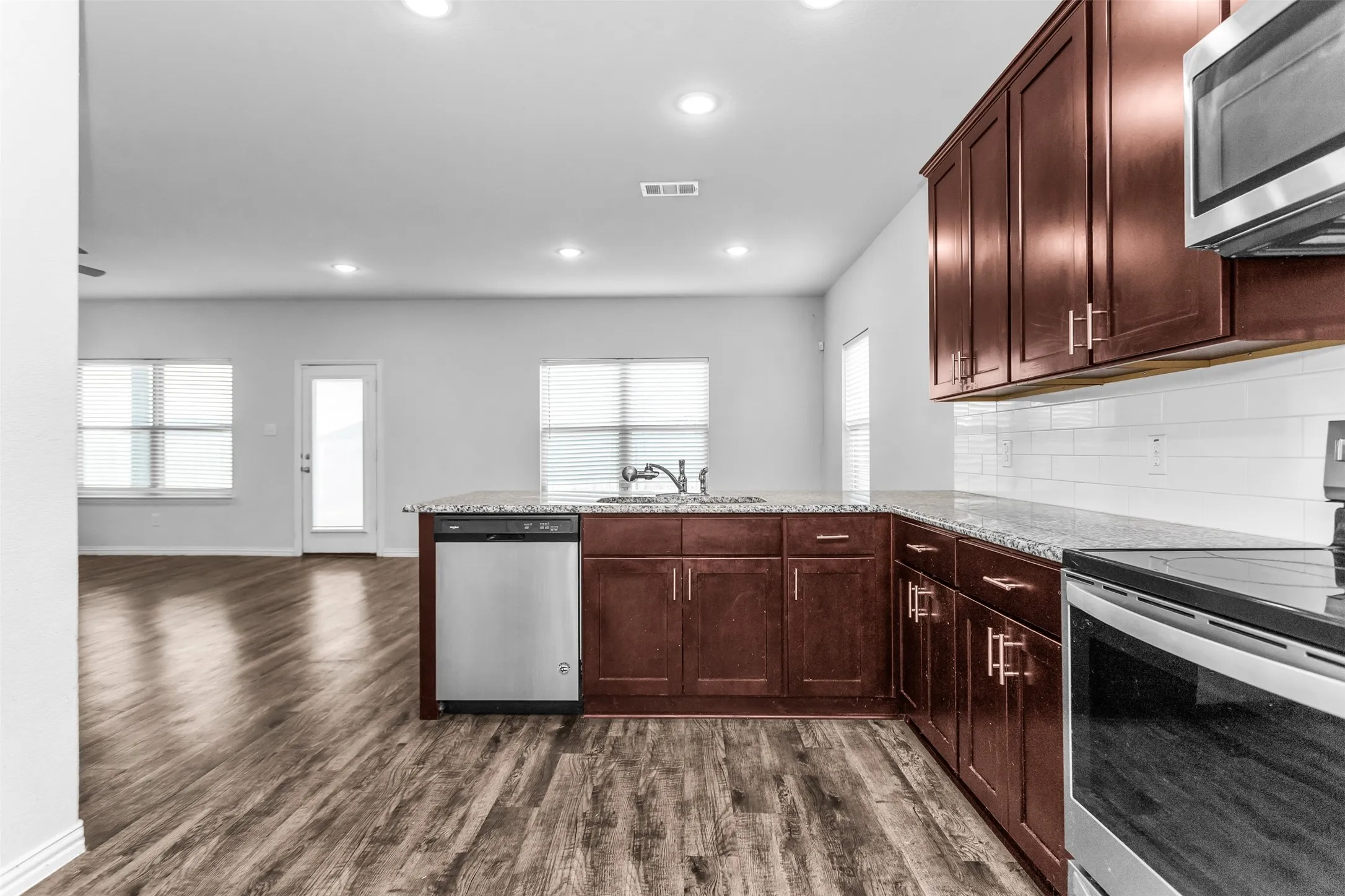 Kitchen featuring wood-finish flooring, dark wood cabinetry, light-toned countertops, a stainless steel dishwasher, and a built-in microwave