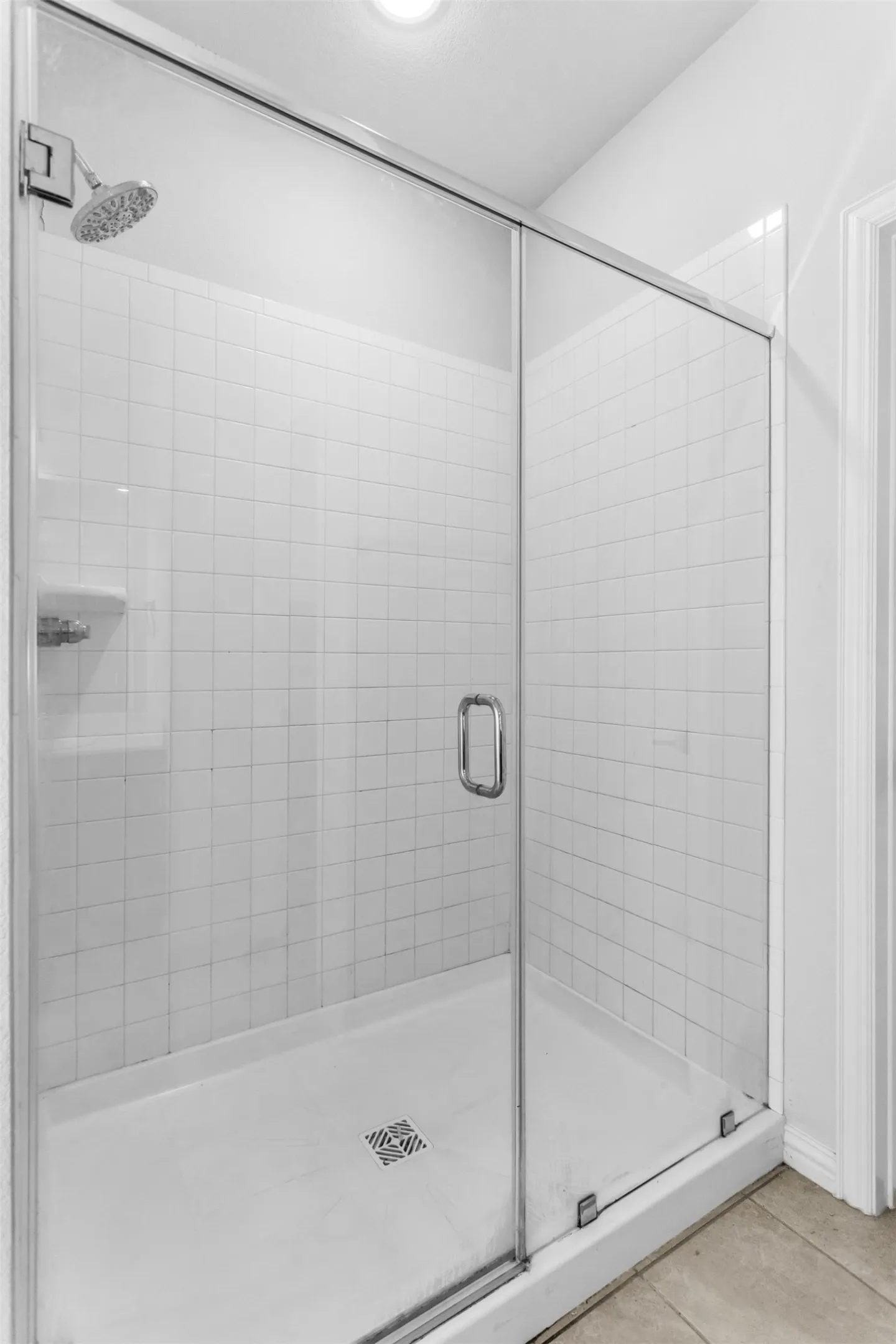 Glass-enclosed shower featuring white square tile surround, a built-in soap niche, and a chrome shower head