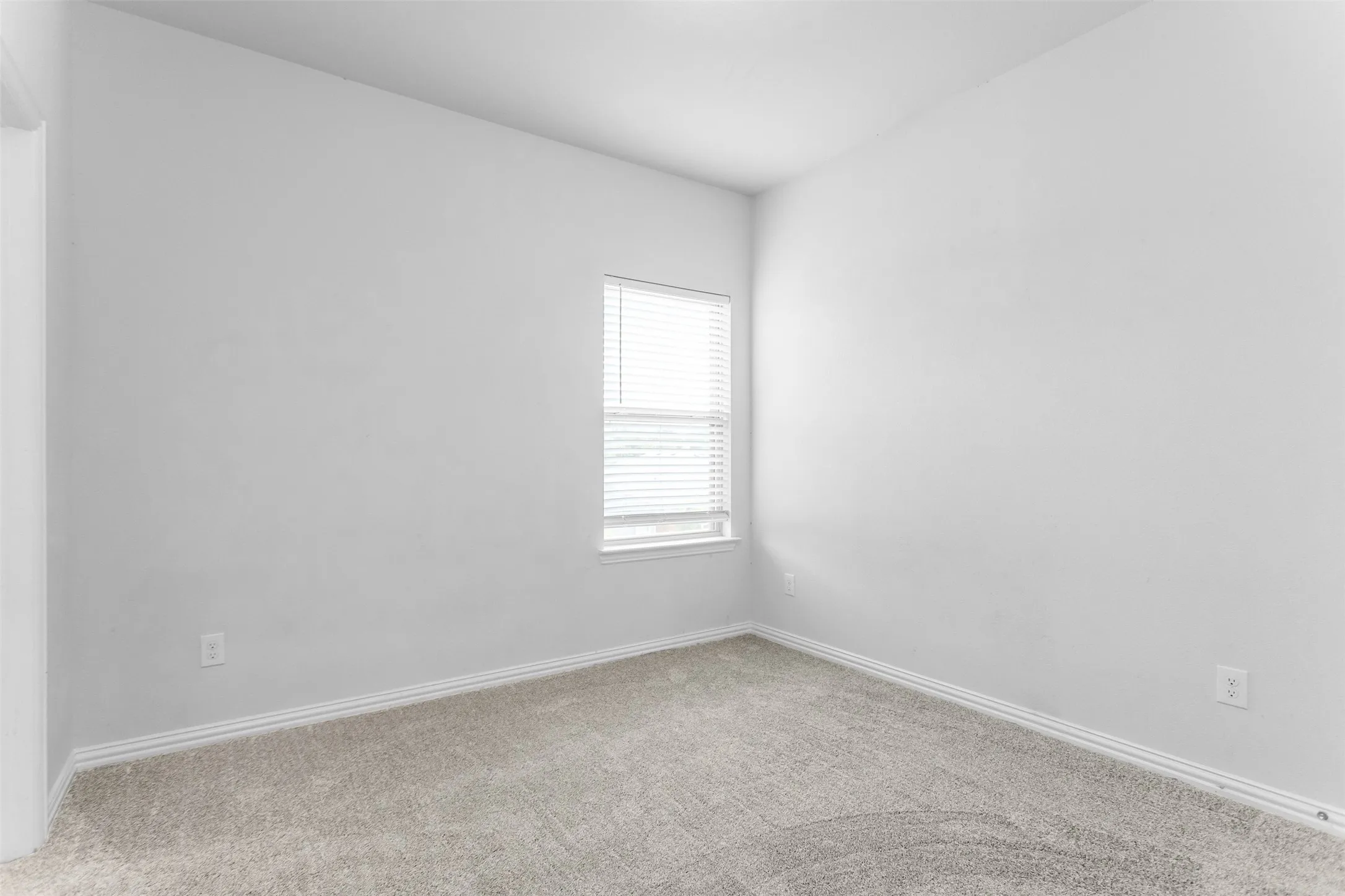 Light gray walls with a single window featuring blinds, complemented by gray carpeting