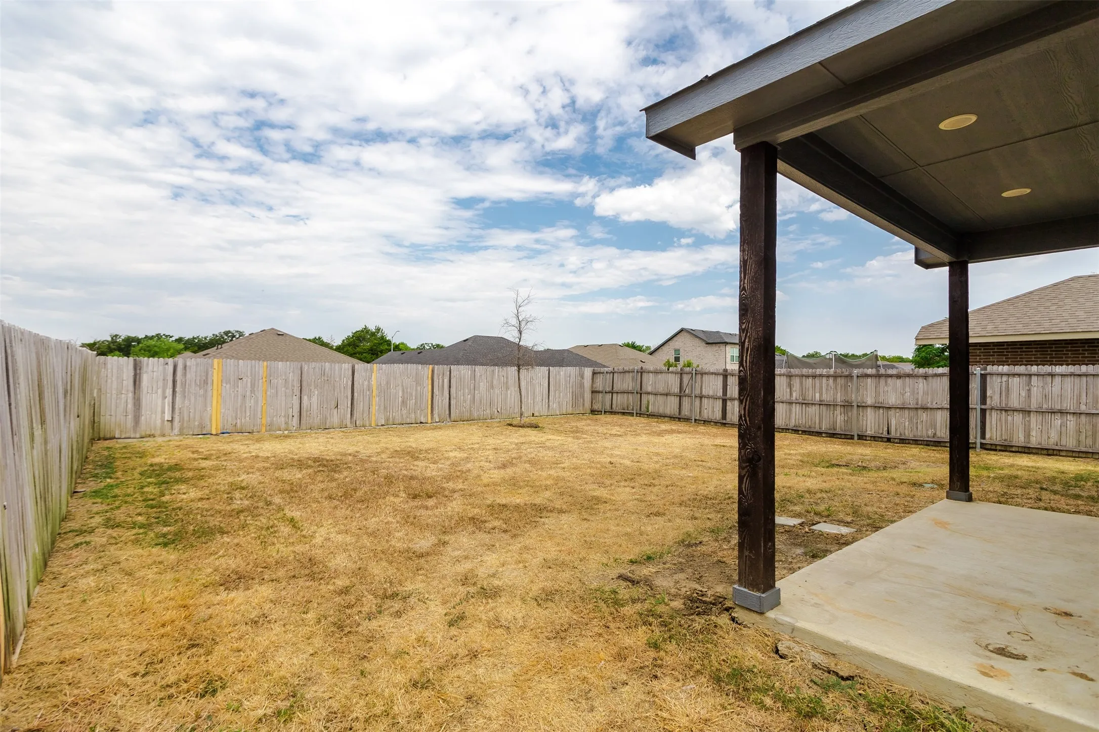 Fenced backyard with concrete patio featuring recessed lighting and robust support columns