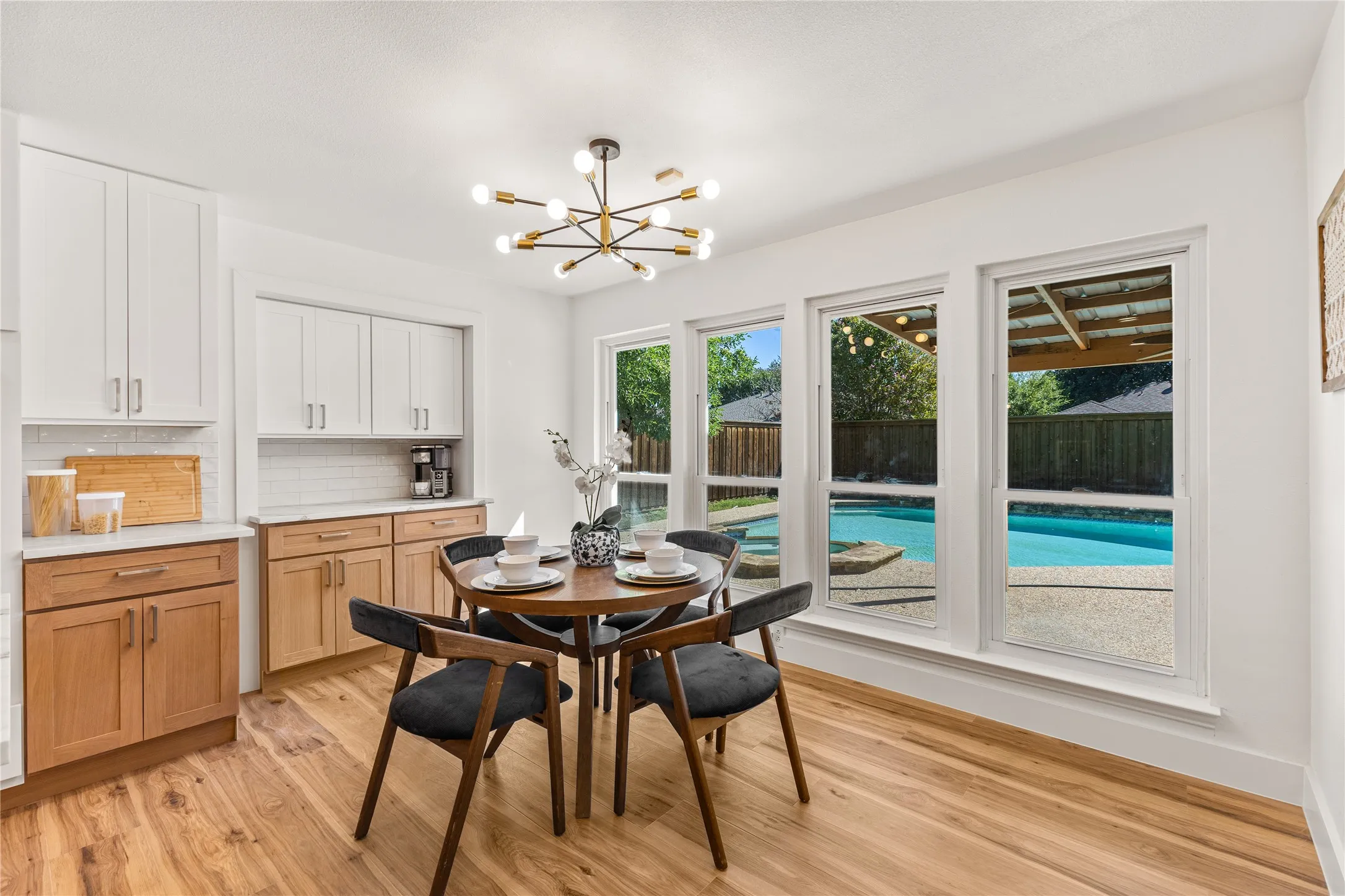 Wood-finish flooring, white upper cabinetry, light wood-finish lower cabinetry, white subway tile backsplash, and a modern light fixture