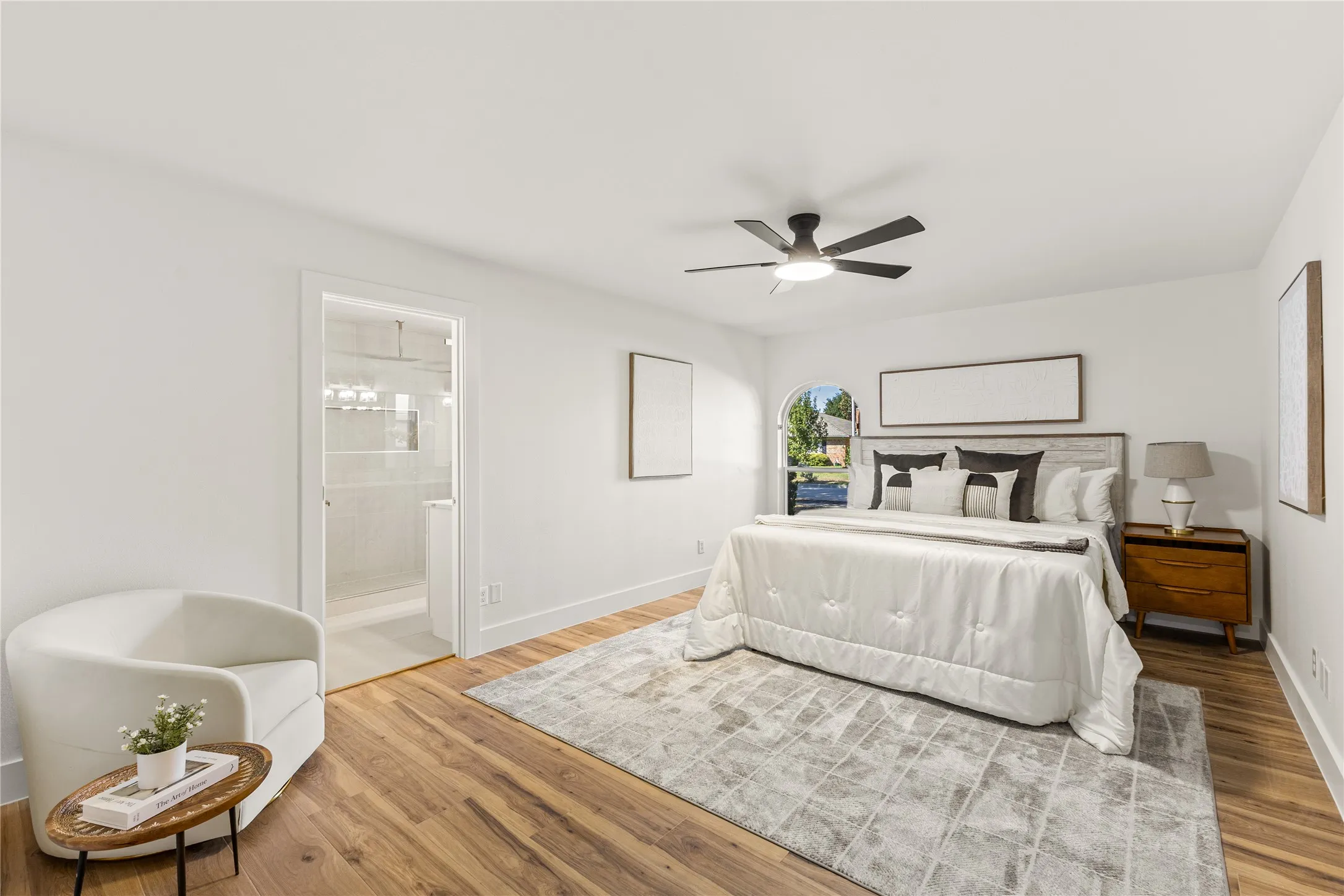 Wood-finish flooring, overhead ceiling fan, arched window, and an en-suite bathroom with a glass-enclosed shower