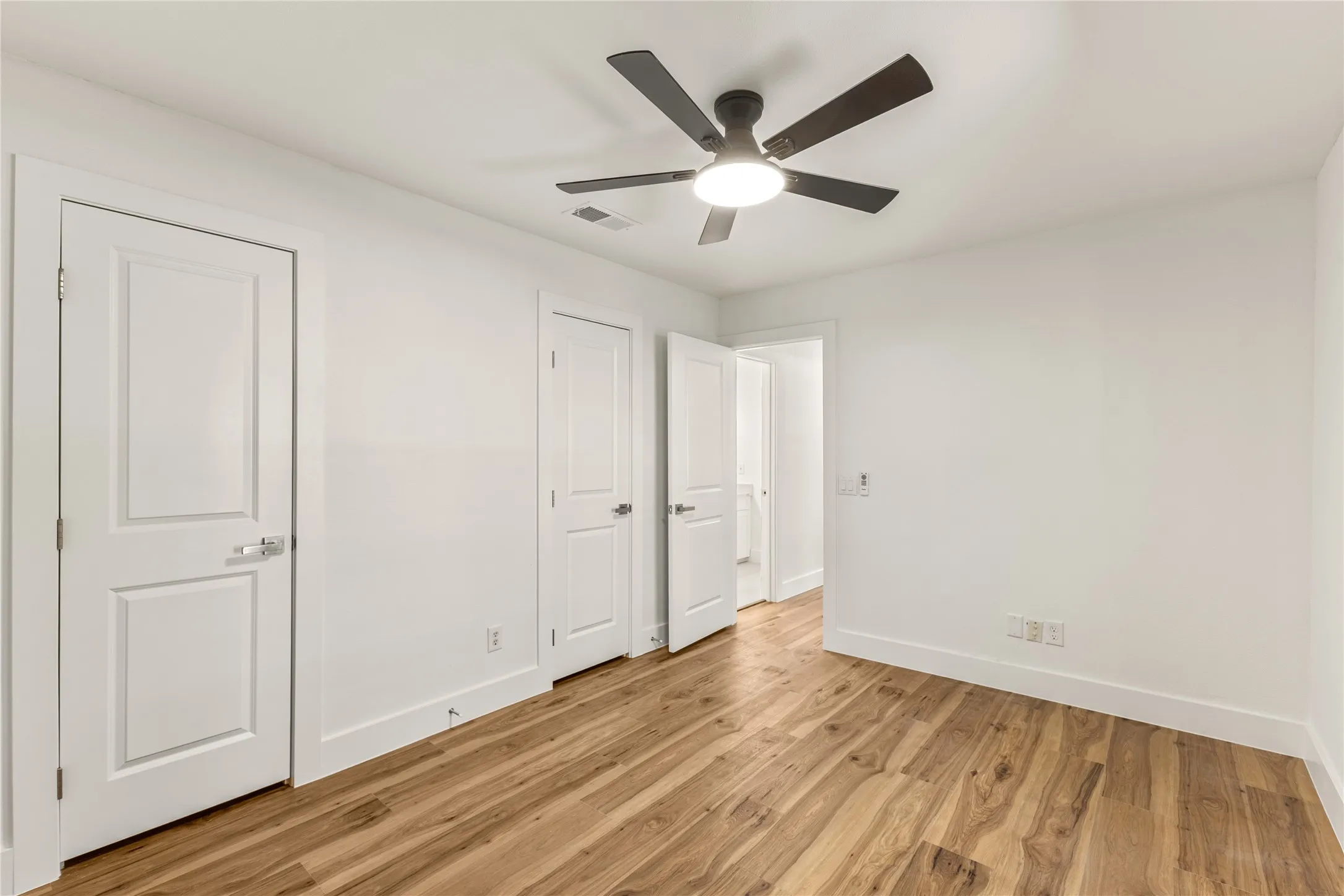Wood-finish flooring, white walls, two-panel interior doors, and a ceiling fan with integrated lighting