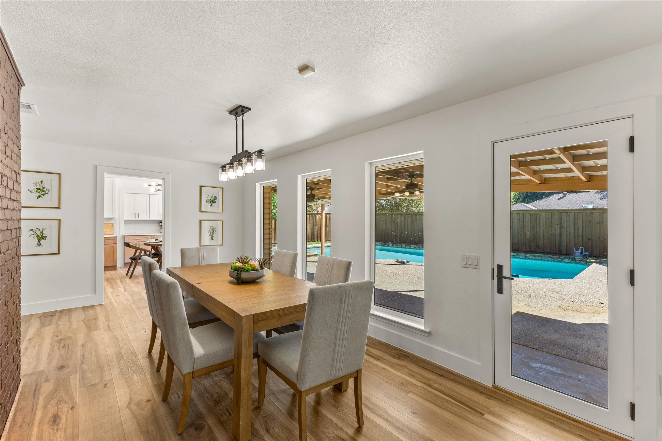 Wood-finish flooring, white walls, exposed brick accent wall, pendant lighting fixture, and a glass-paneled door