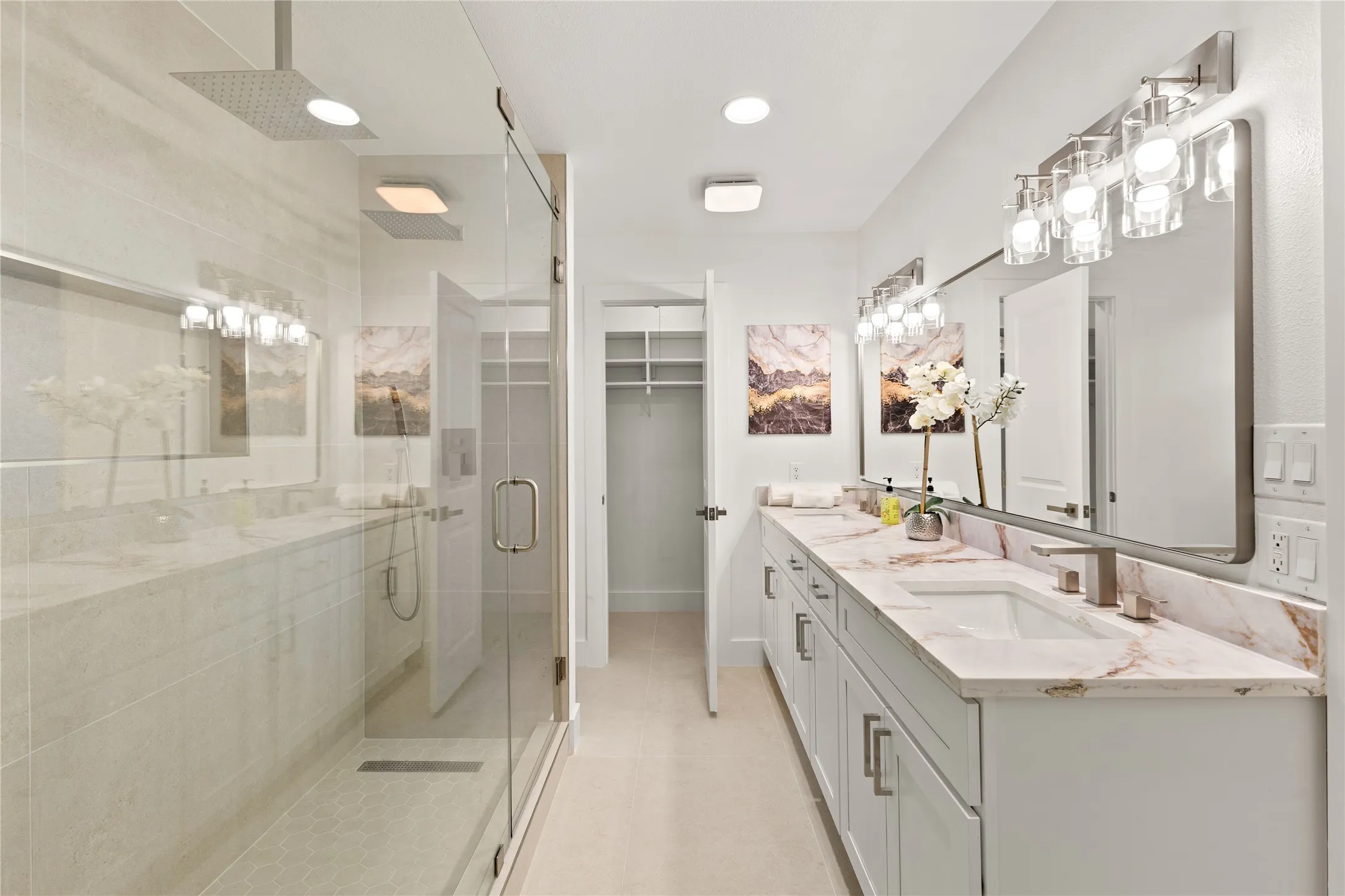 Dual vanity with integrated sinks and stone countertops, glass-enclosed shower with rain showerhead, recessed lighting, and an open closet with built-in shelving