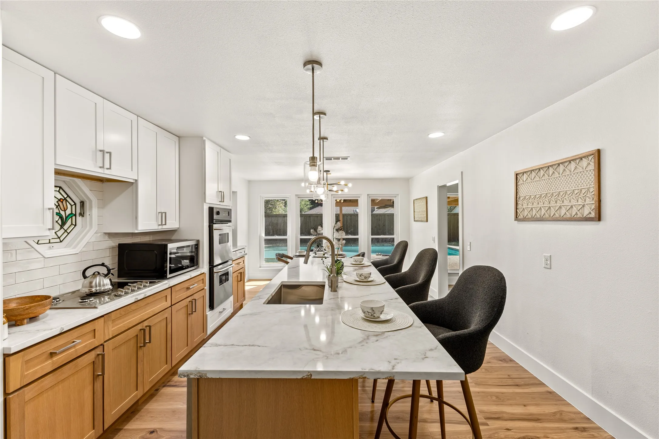 Modern kitchen featuring a large island with seating, a stainless steel sink, dual-tone cabinetry, double wall ovens, and recessed lighting