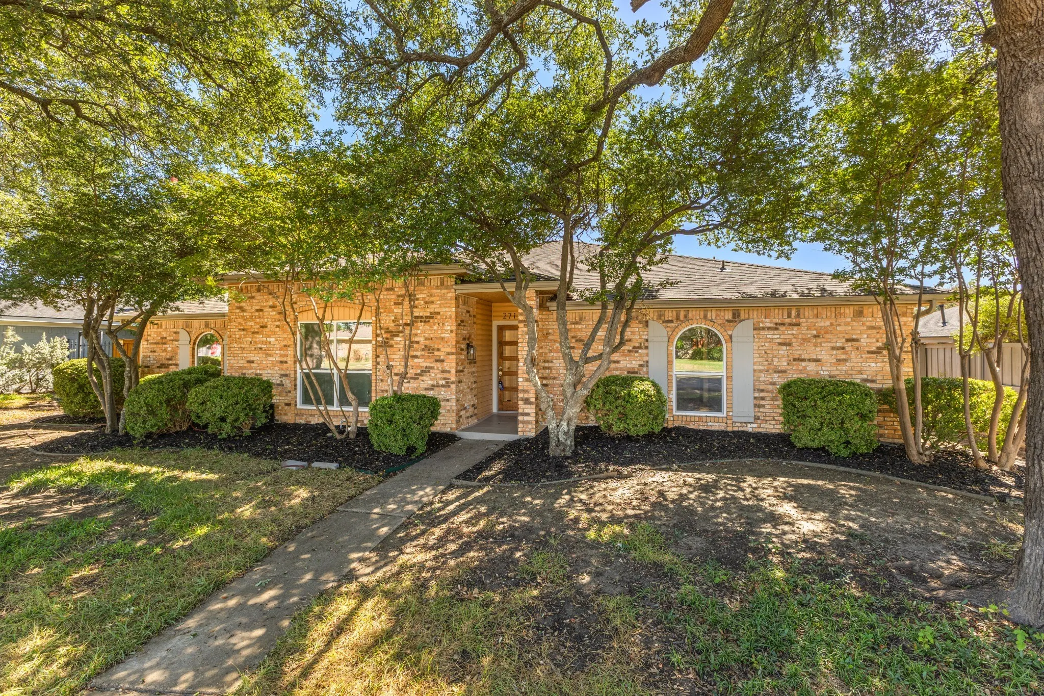Brick exterior featuring an arched window, a covered entryway, and mature landscaping
