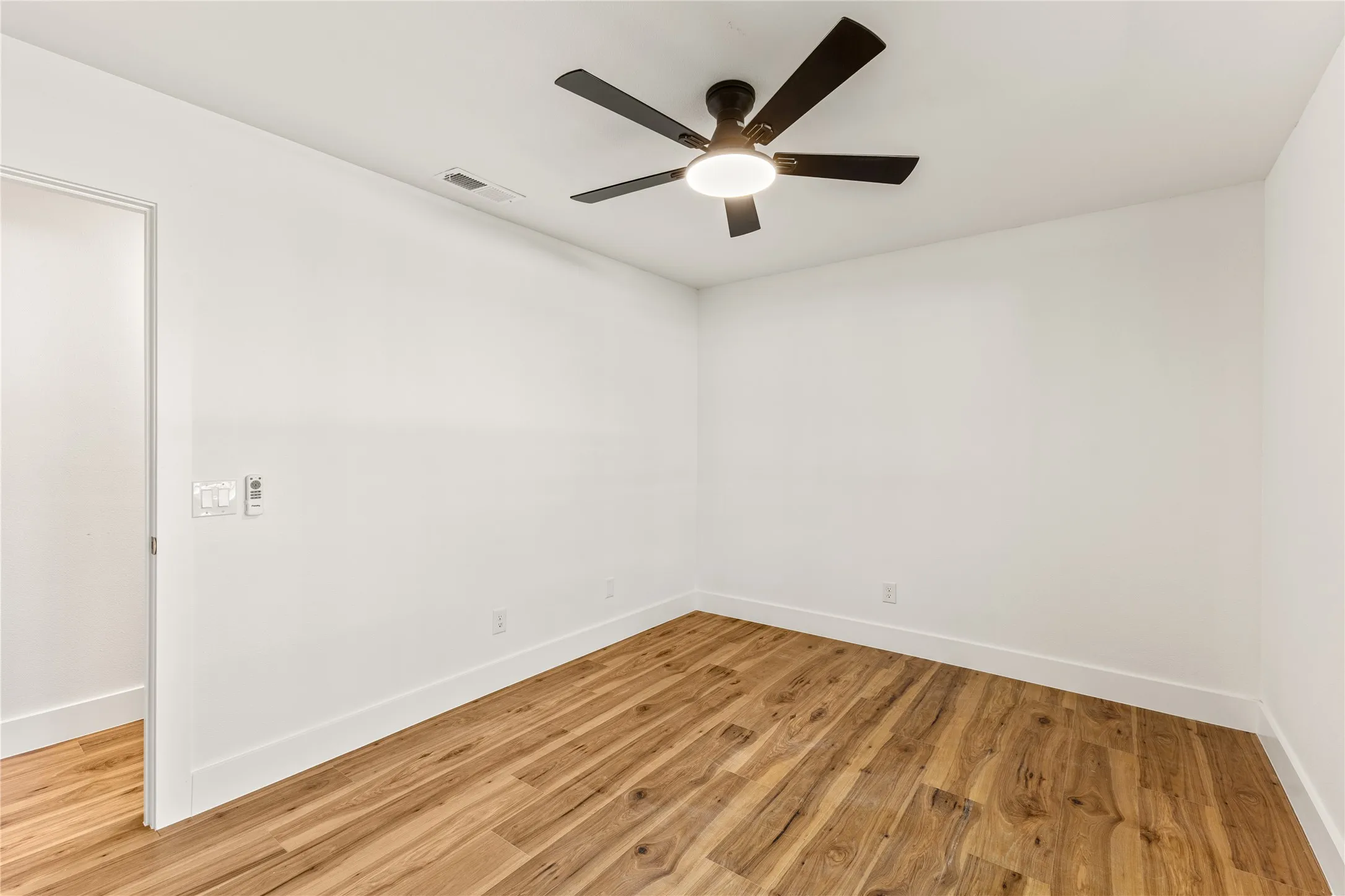 Wood-finish flooring with white walls and a ceiling fan with integrated lighting