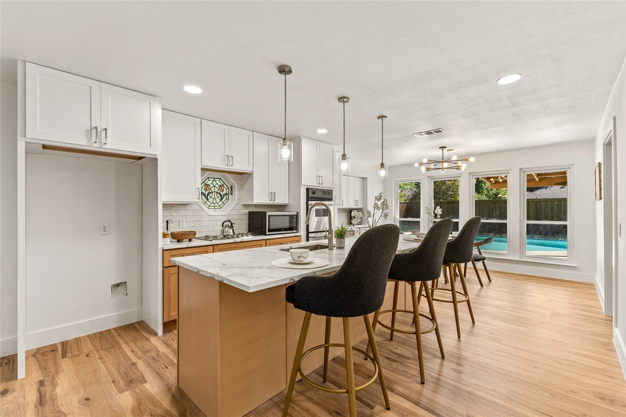 Wood-finish flooring, white cabinetry, island with stone countertop, stainless steel appliances, and multiple windows