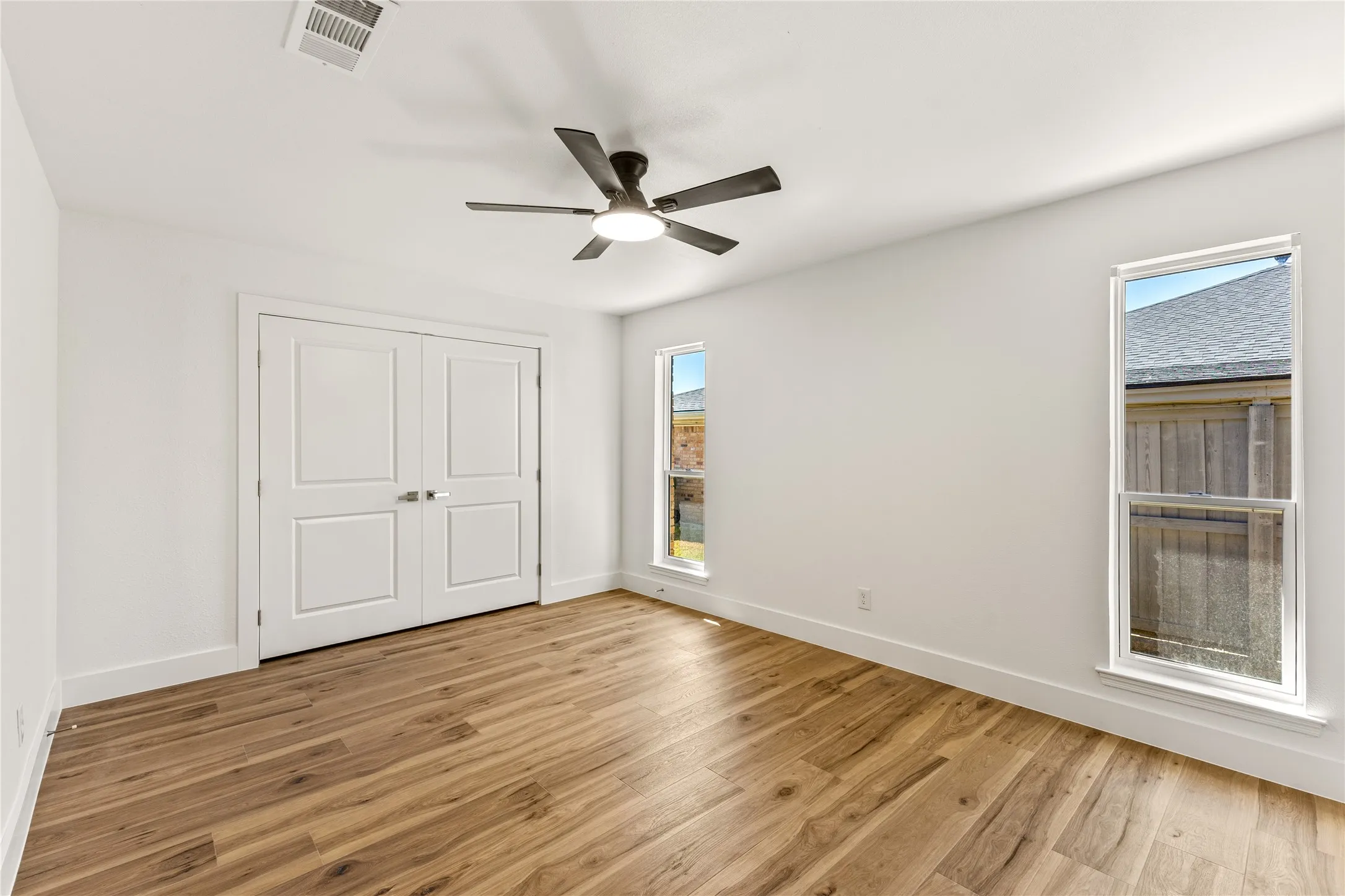 Wood-finish flooring, white walls, and a ceiling fan with integrated lighting