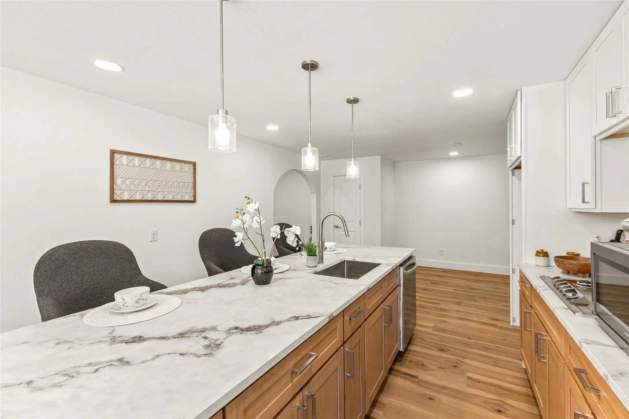 Kitchen with a large island featuring a stone countertop, recessed lighting, wood-finish flooring, and pendant light fixtures
