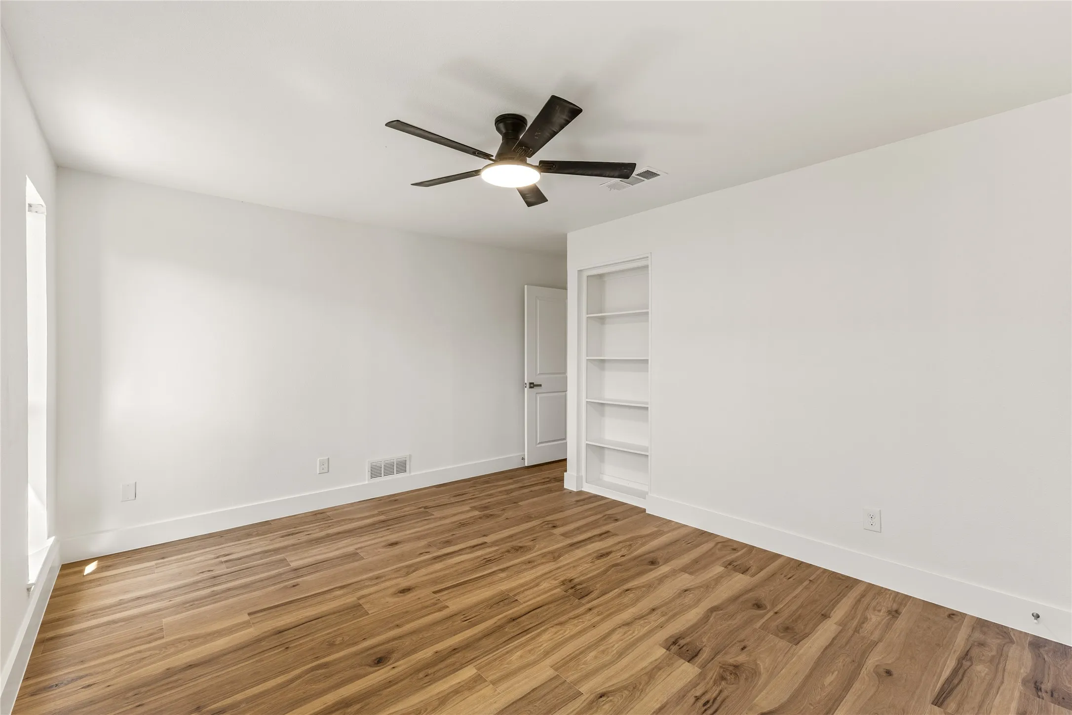Wood-finish flooring, built-in shelving, white walls, modern ceiling fan, and white trim