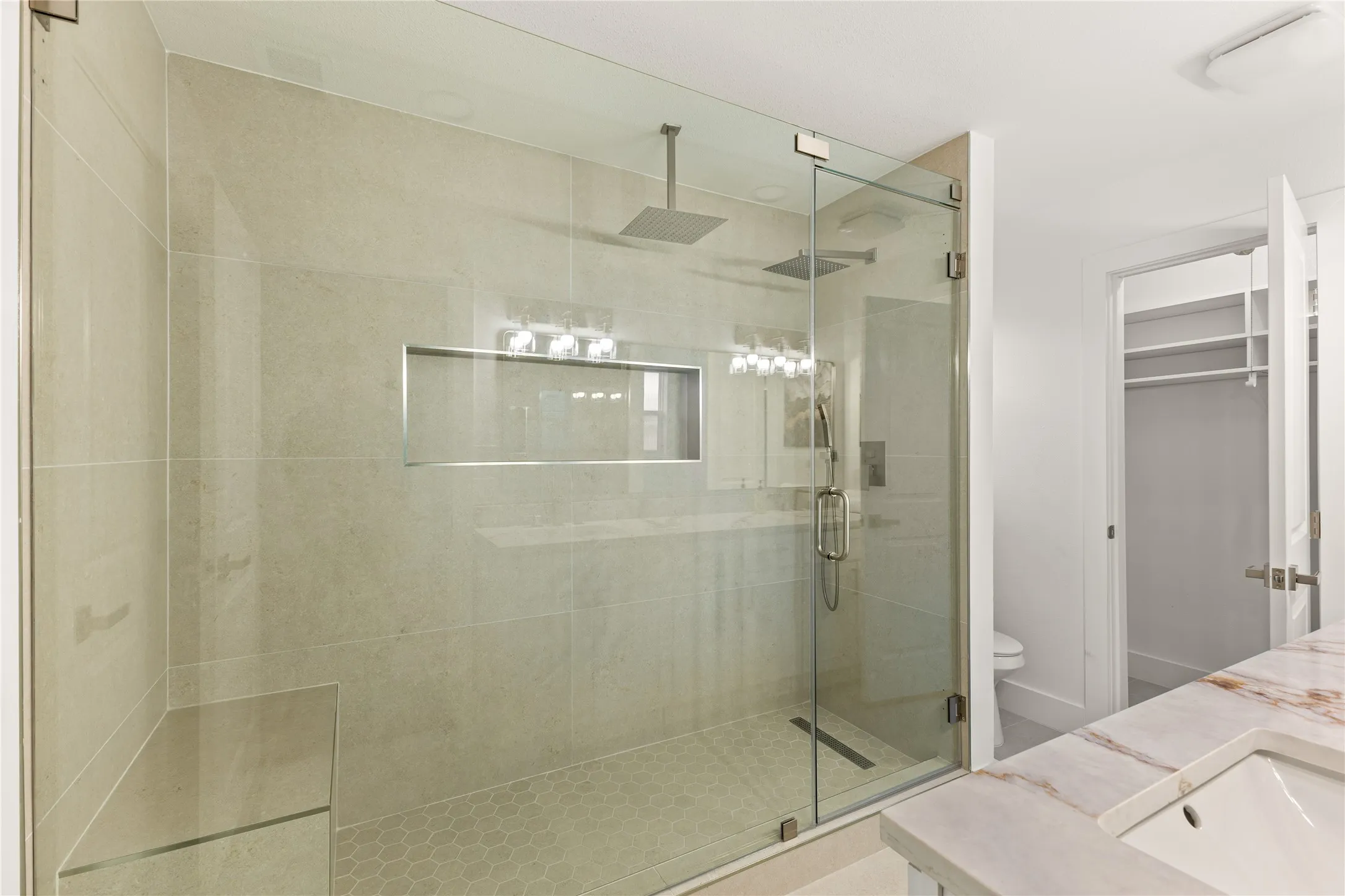Glass-enclosed shower with a built-in bench, dual rain shower heads, and recessed niche