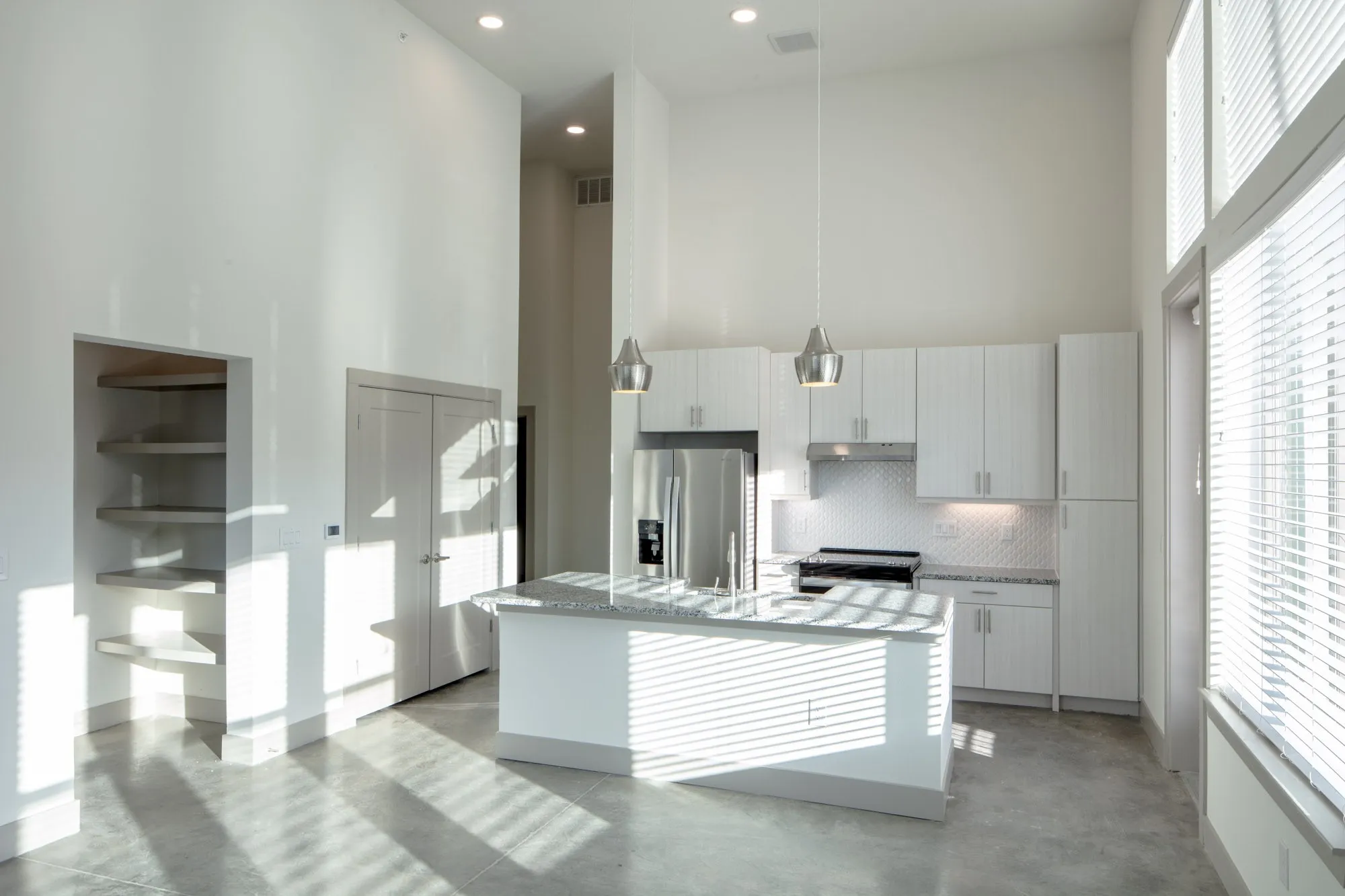 Kitchen with appliances with stainless steel finishes, a kitchen island with sink, a towering ceiling, and a wealth of natural light