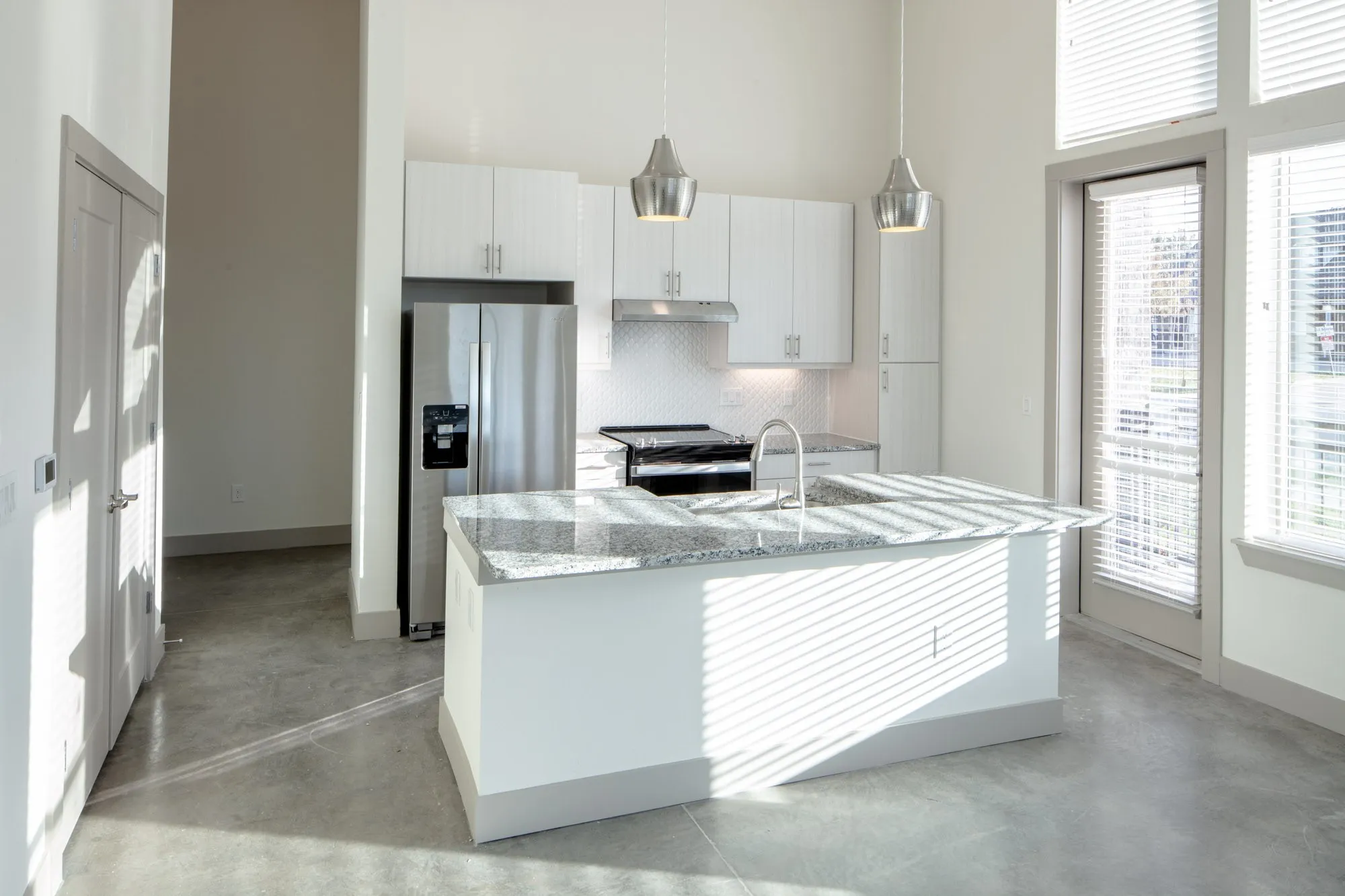 Kitchen featuring white cabinets, hanging light fixtures, tasteful backsplash, stainless steel appliances, and a high ceiling