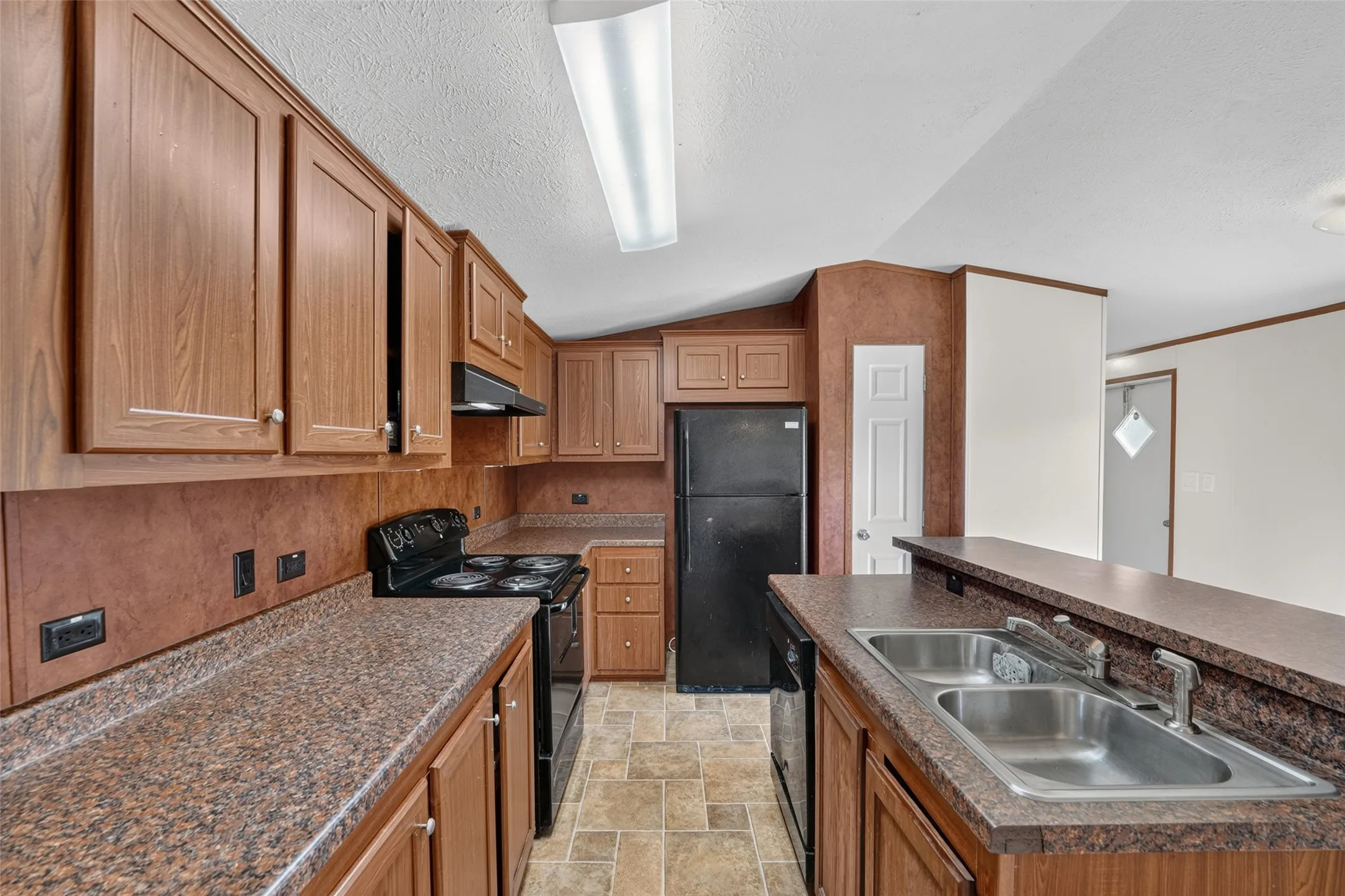 Kitchen featuring wood-finish cabinetry, granite-style countertops, a stainless steel double sink, and a black appliance suite
