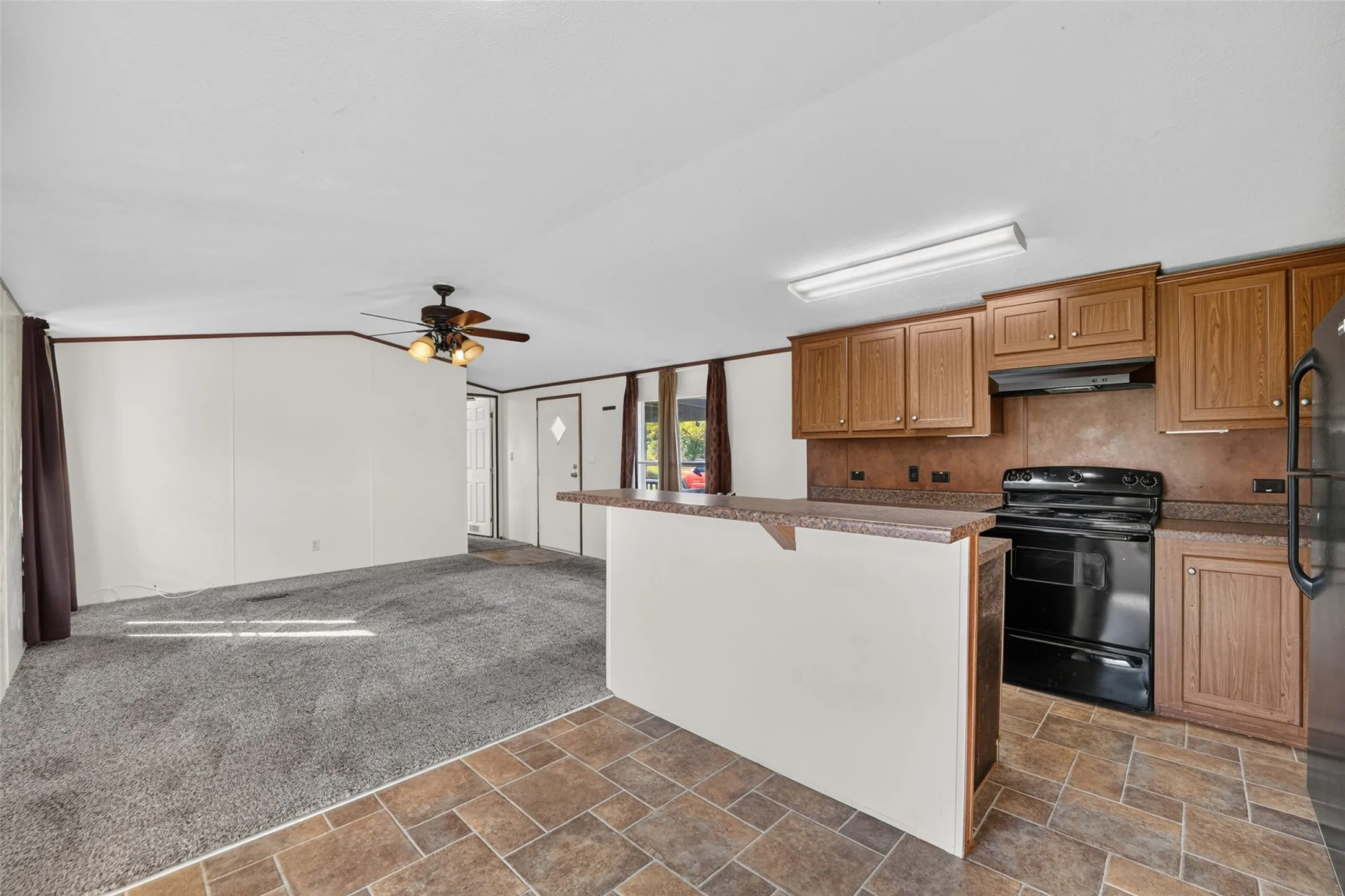 Kitchen and living area featuring a ceiling fan, wood-finish cabinetry, black appliances, and a breakfast bar