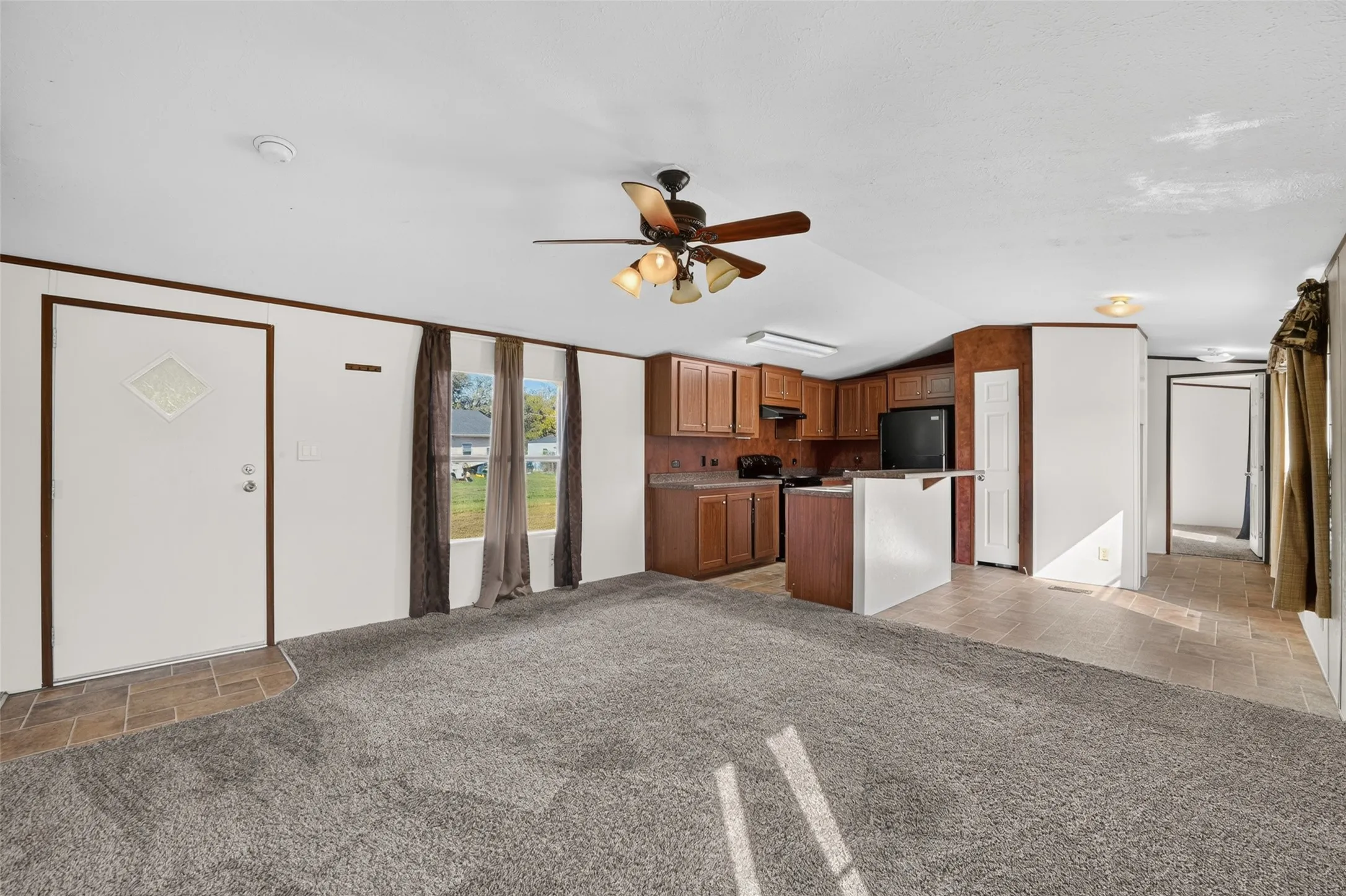 Open-concept living space featuring wood-finish cabinetry, a black appliance package, a ceiling fan, and carpeted flooring