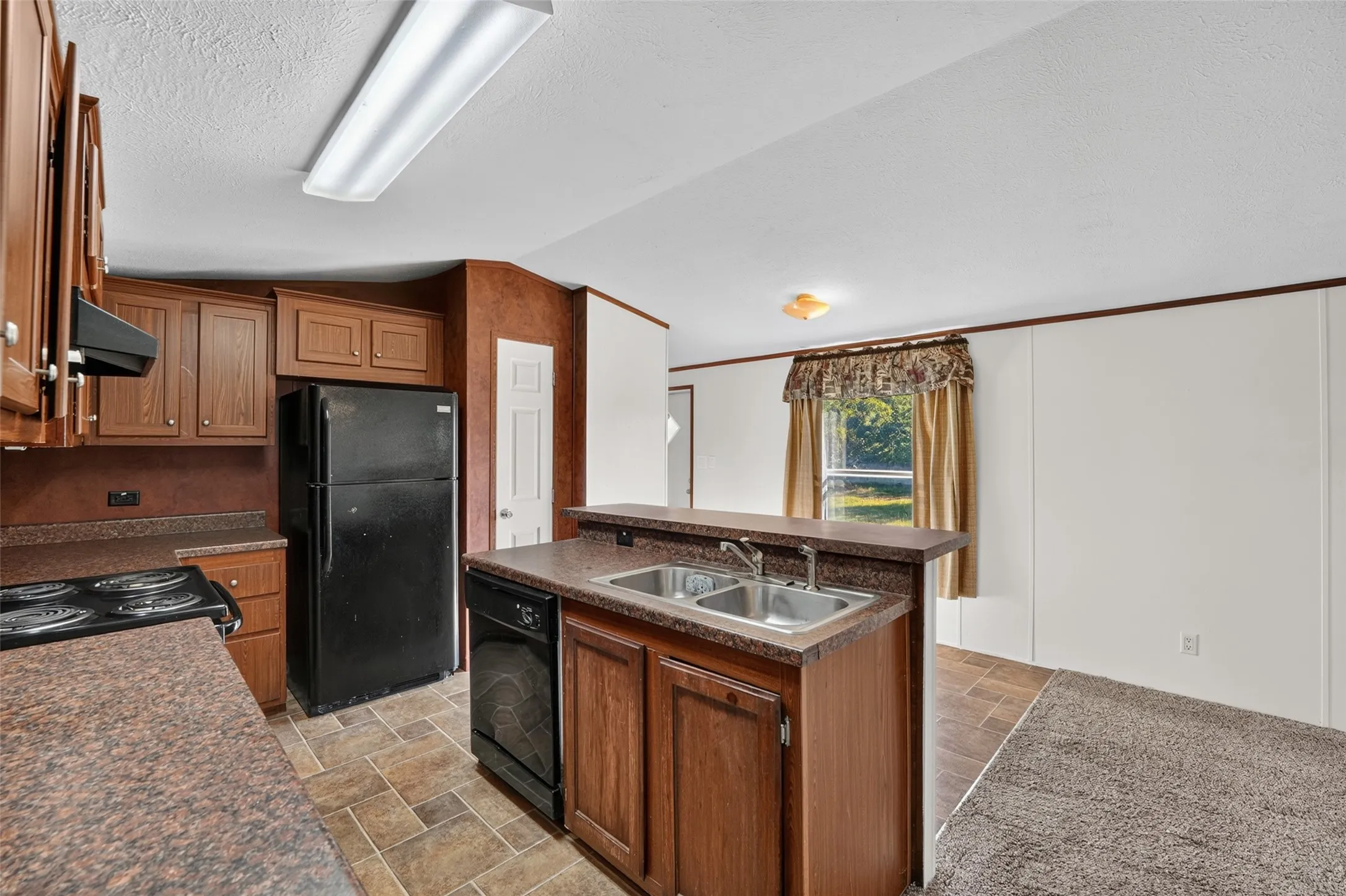 Kitchen featuring wood-finish cabinetry, a double basin stainless steel sink, black appliances, and a pass-through bar