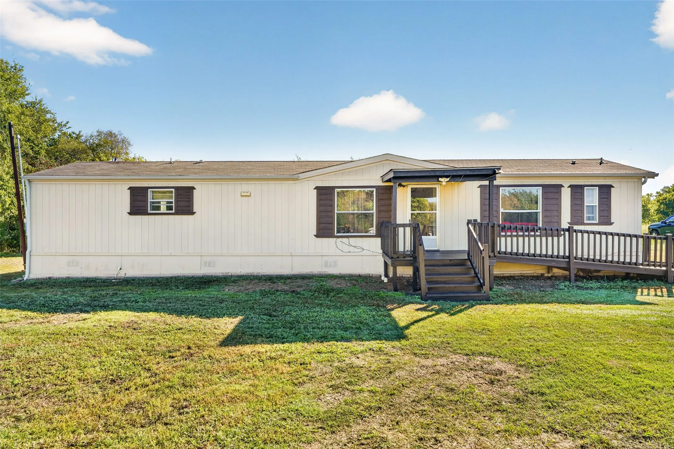 Cream-colored exterior siding with brown shutters, dark wood-finish deck with railings, and an accessible ramp