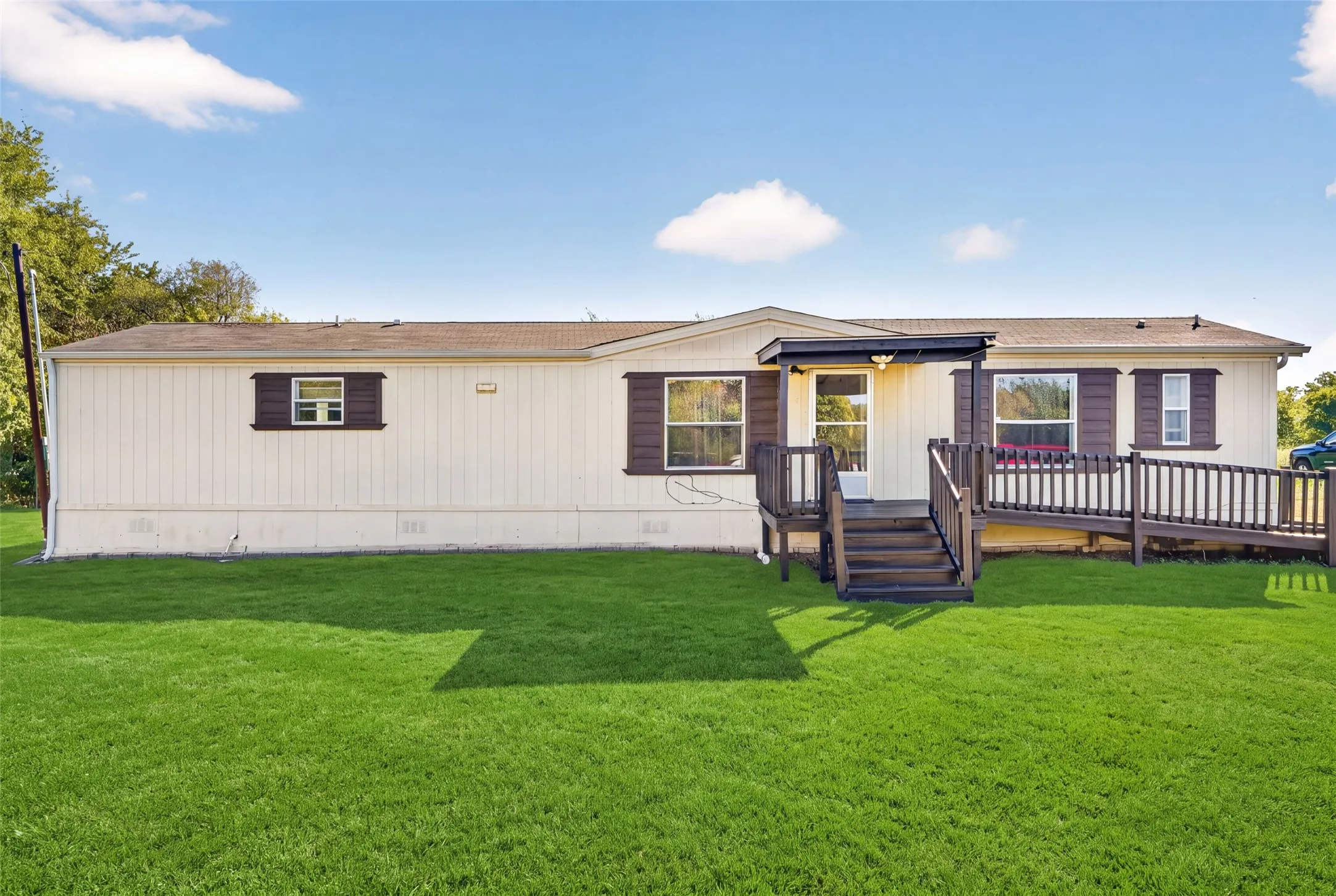 Cream siding with contrasting brown shutters, an inviting front porch with stairs, and an integrated ramp for accessibility