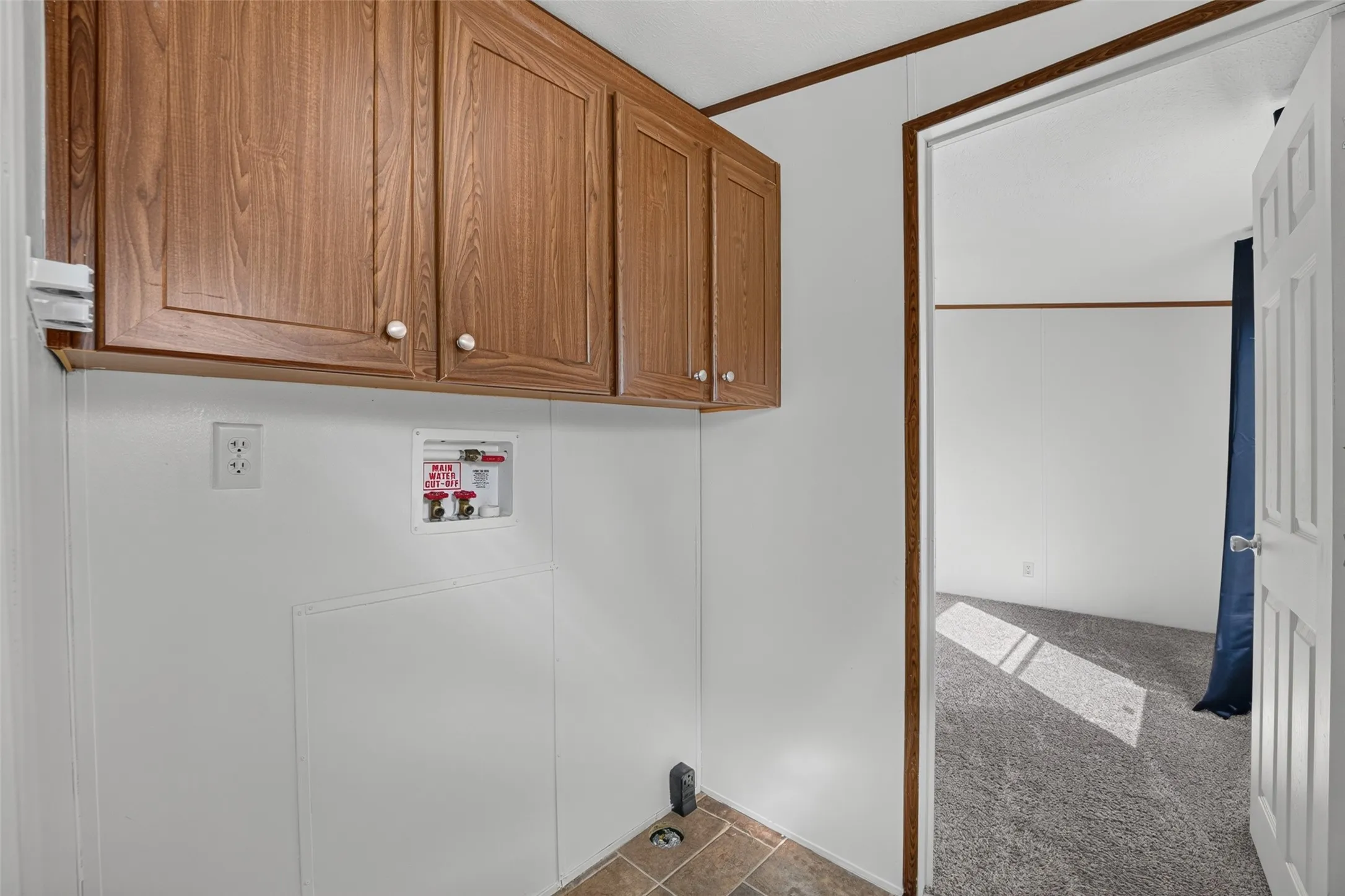 Laundry area with upper wood-finish cabinetry, utility hookups, and durable flooring