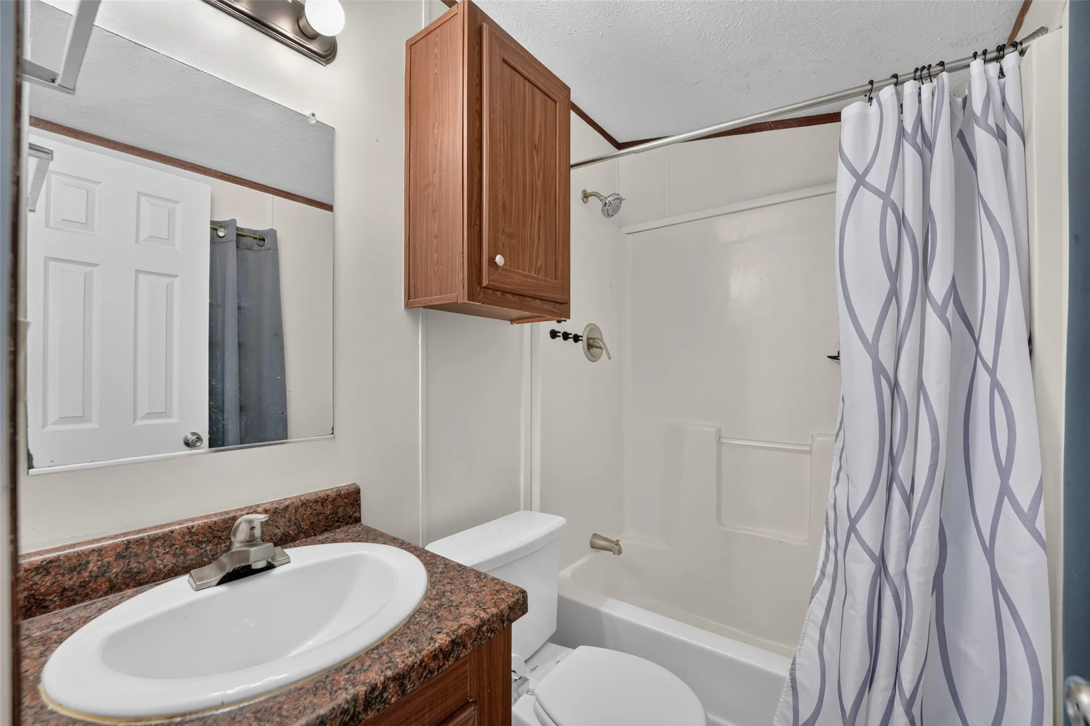 Bathroom featuring a vanity with an integrated sink, a dark countertop, an overhead wall-mounted cabinet, a toilet, and a shower/tub combination