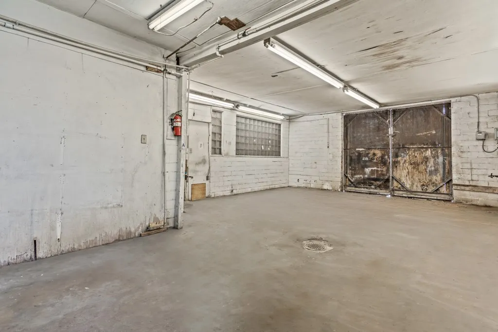 Concrete flooring with exposed brick walls, industrial ceiling lighting, and large metal doors