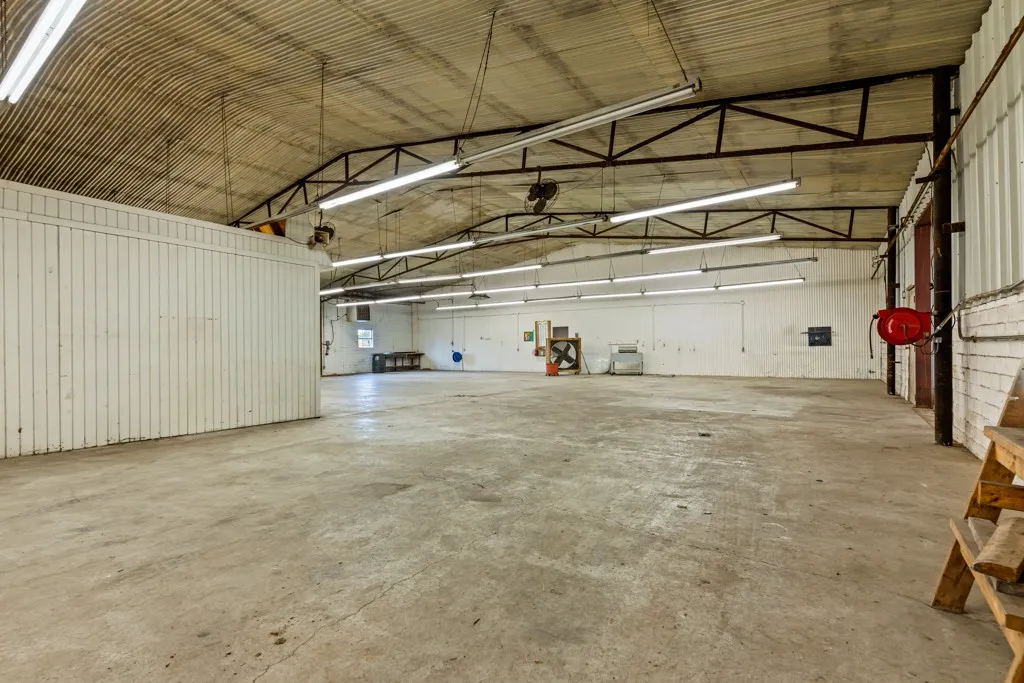 Concrete flooring, corrugated metal ceiling, exposed structural beams, fluorescent lighting fixtures, and painted panel walls