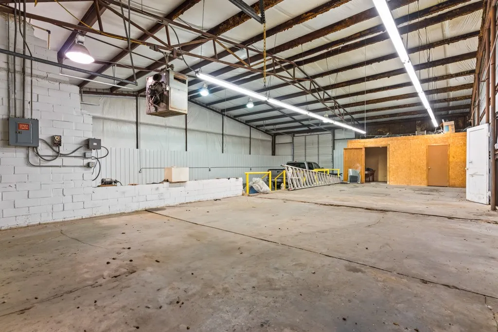 Concrete flooring, exposed metal ceiling trusses, fluorescent strip lighting, white brick wall, built-in storage area