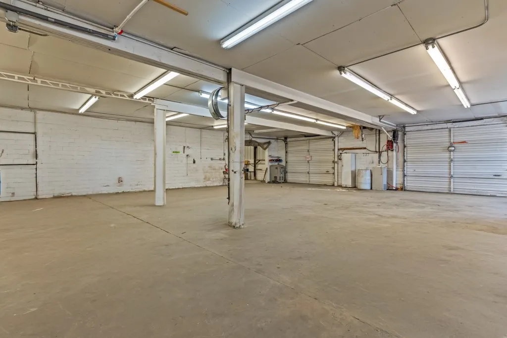 Spacious interior with concrete flooring, multiple overhead fluorescent light fixtures, and several roll-up garage doors