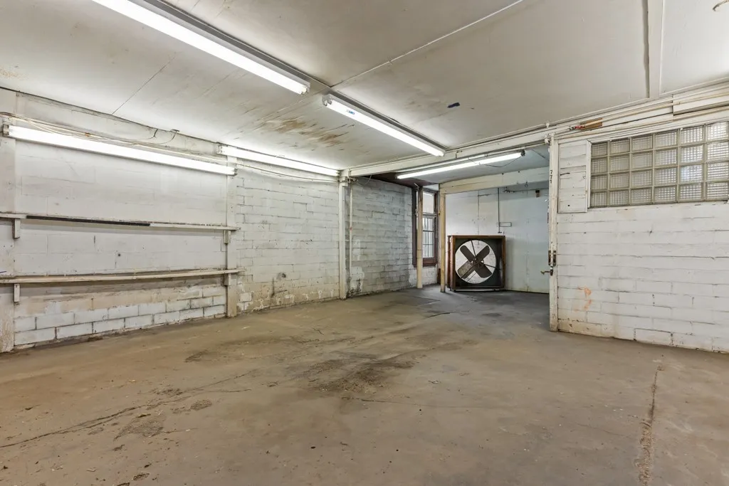 Concrete flooring with painted brick walls, exposed fluorescent lighting, and a large industrial fan