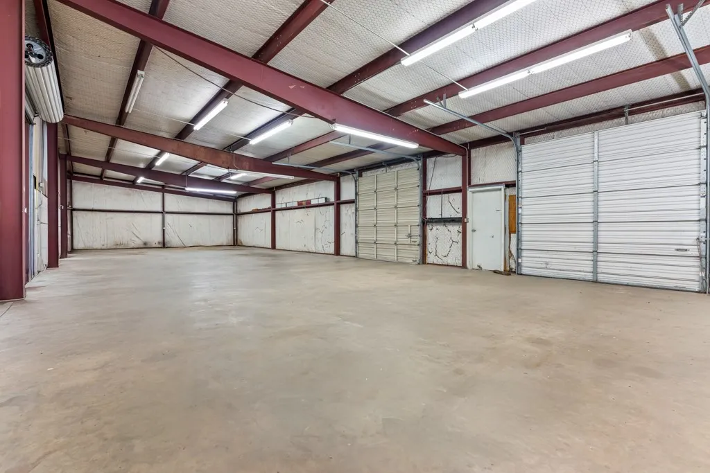 Spacious interior featuring a concrete floor, exposed metal beam construction, multiple overhead lighting fixtures, and several roll-up doors