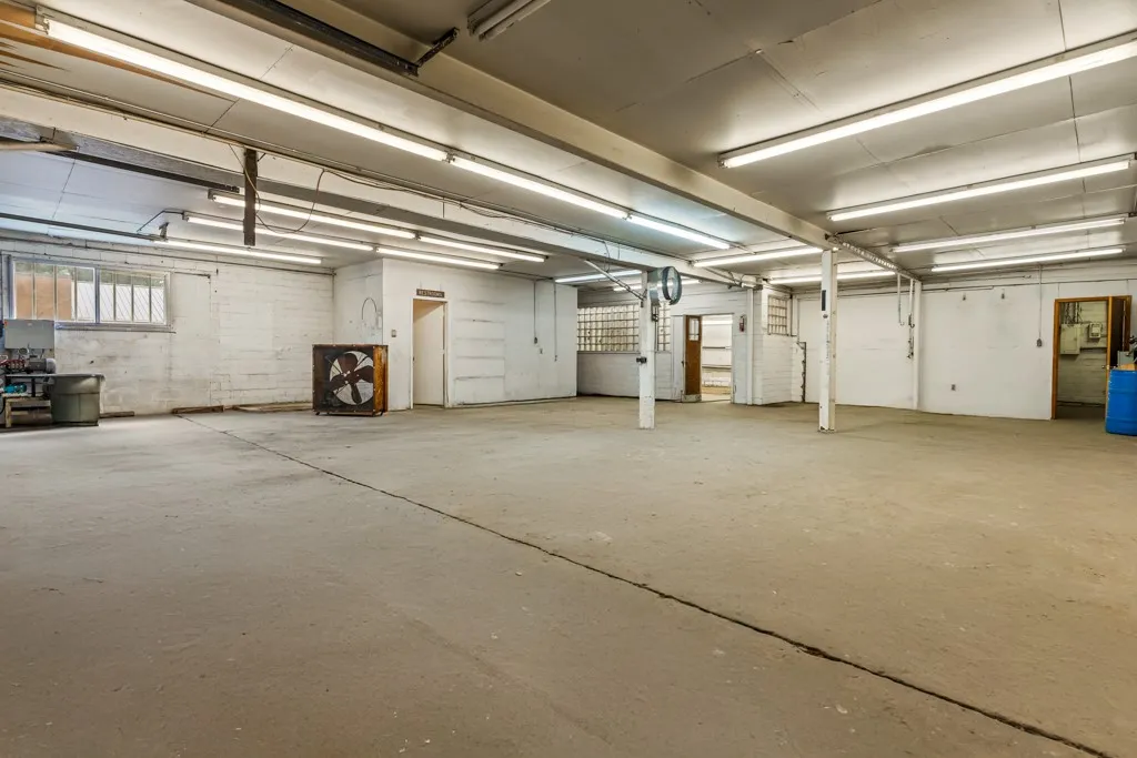 Expansive open space with concrete flooring, exposed overhead fluorescent lighting, and multiple structural support pillars