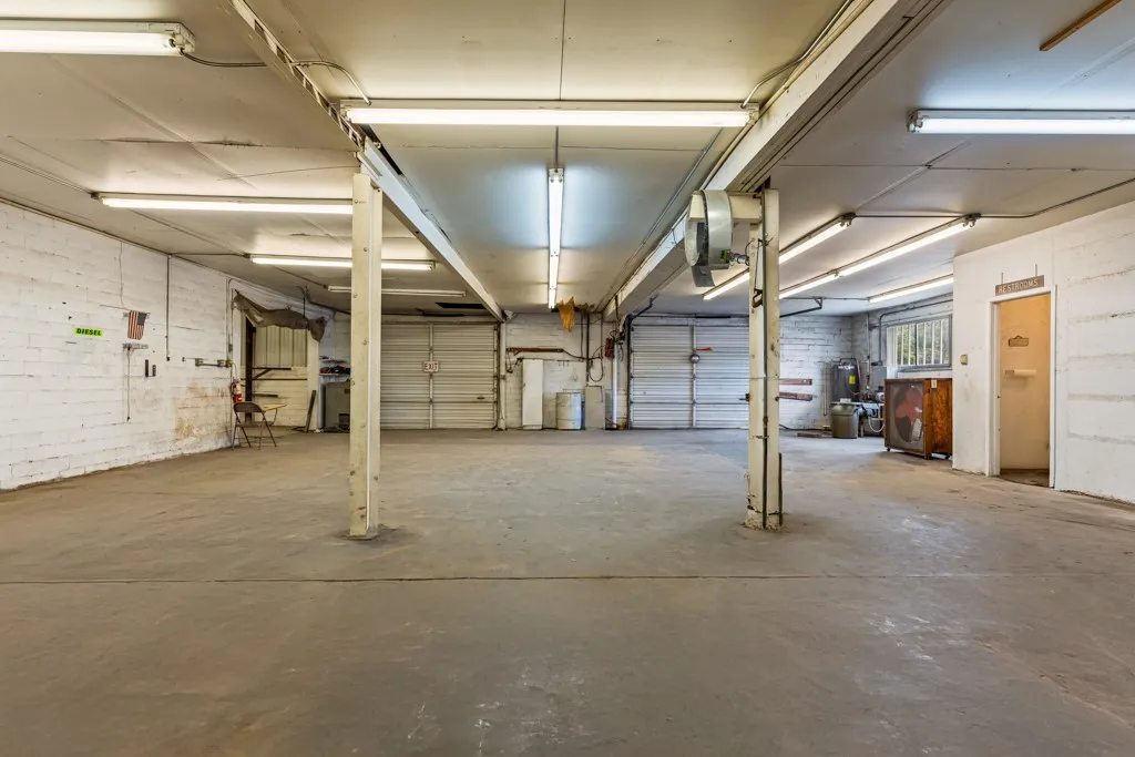 Spacious interior featuring concrete flooring, white brick walls, multiple overhead fluorescent light fixtures, and two overhead garage doors