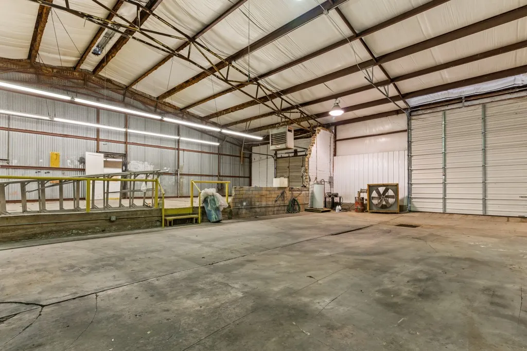 Expansive concrete floor, industrial lighting fixtures, metal roll-up door, loading dock with yellow handrails, and exposed steel truss ceiling