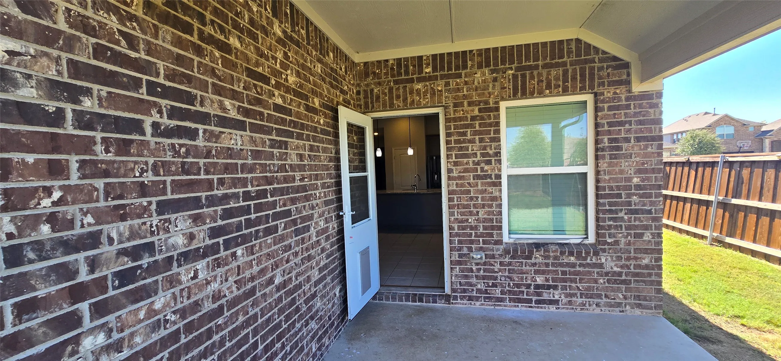 Covered patio with brick exterior, concrete flooring, and a wood privacy fence