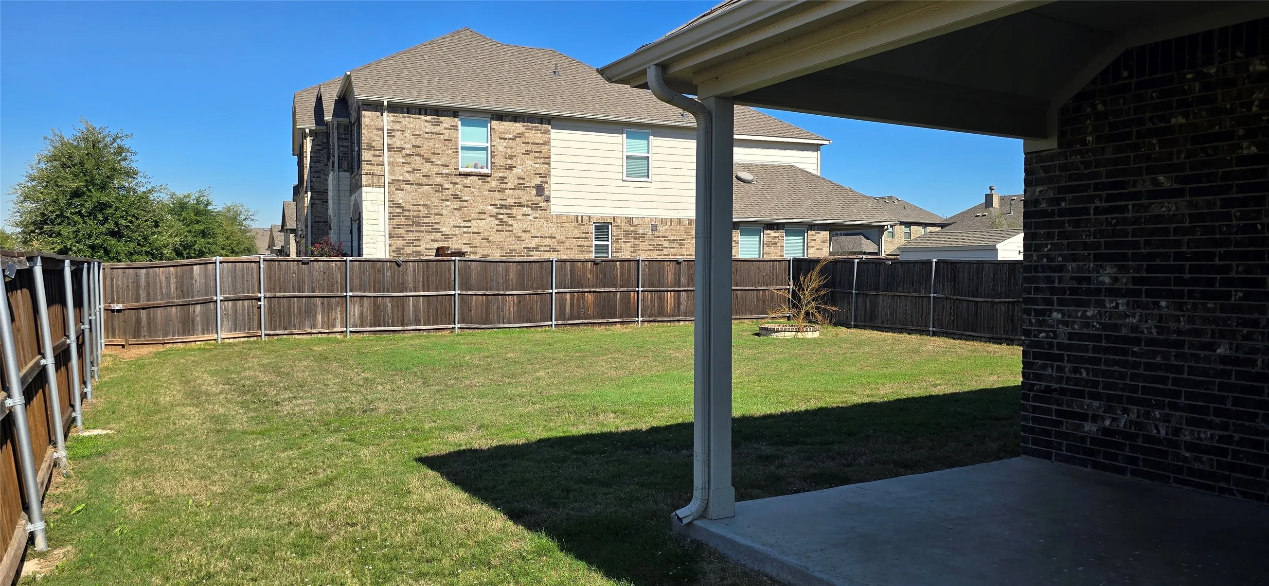 Expansive backyard featuring a manicured lawn, full wood privacy fencing, and a covered concrete patio