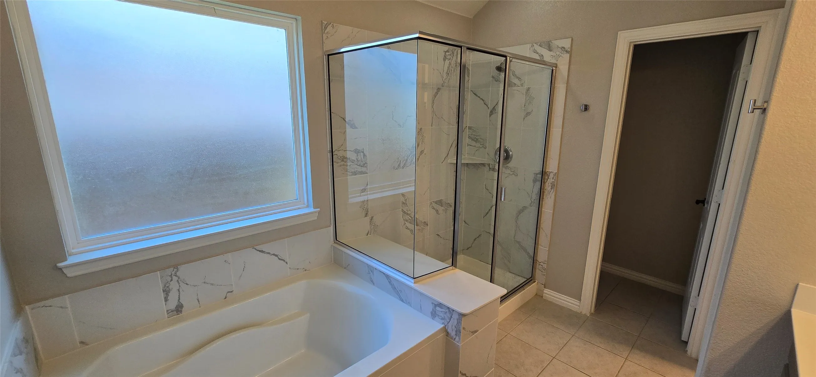 Tiled shower enclosure with clear glass door, separate soaking tub, and privacy window