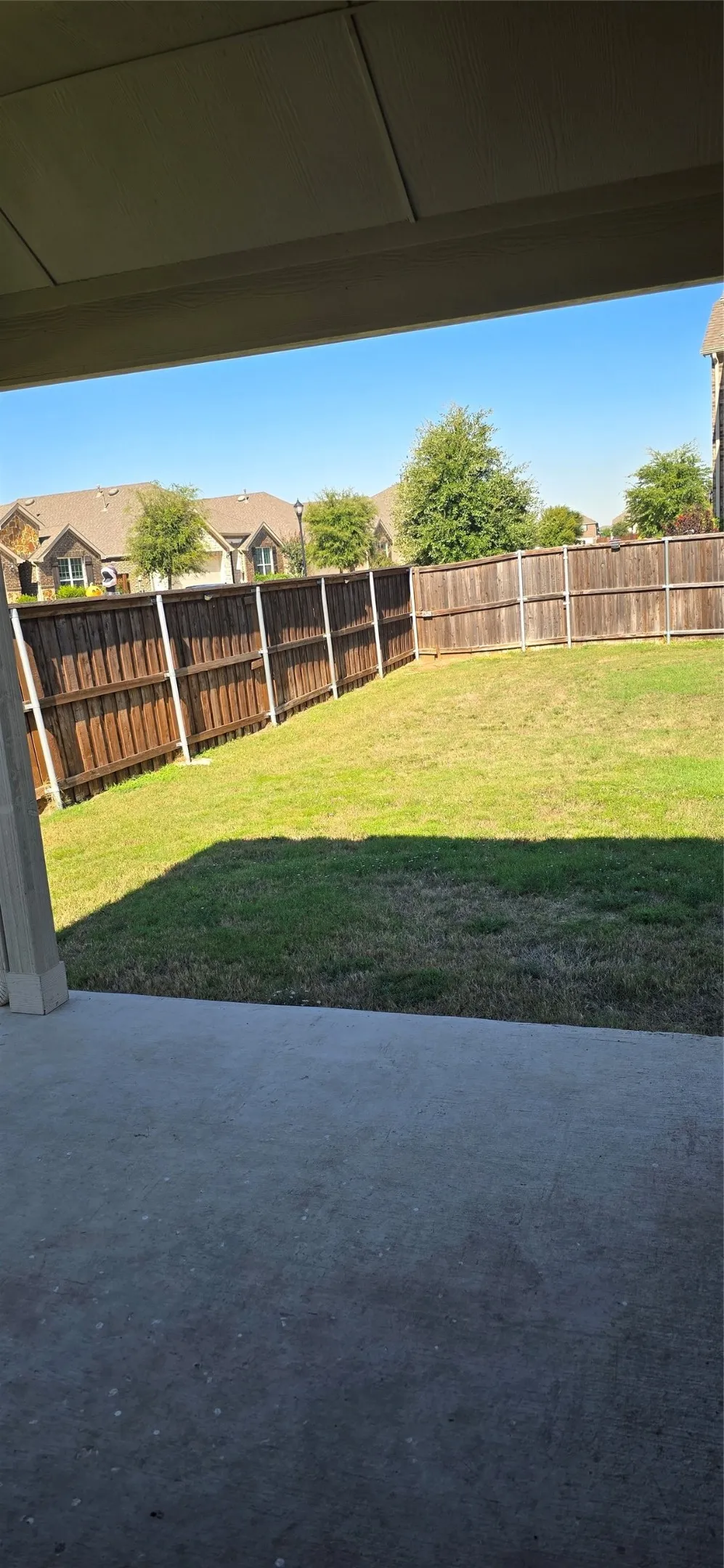 Expansive backyard featuring a stained wood privacy fence, mature trees, and a concrete patio