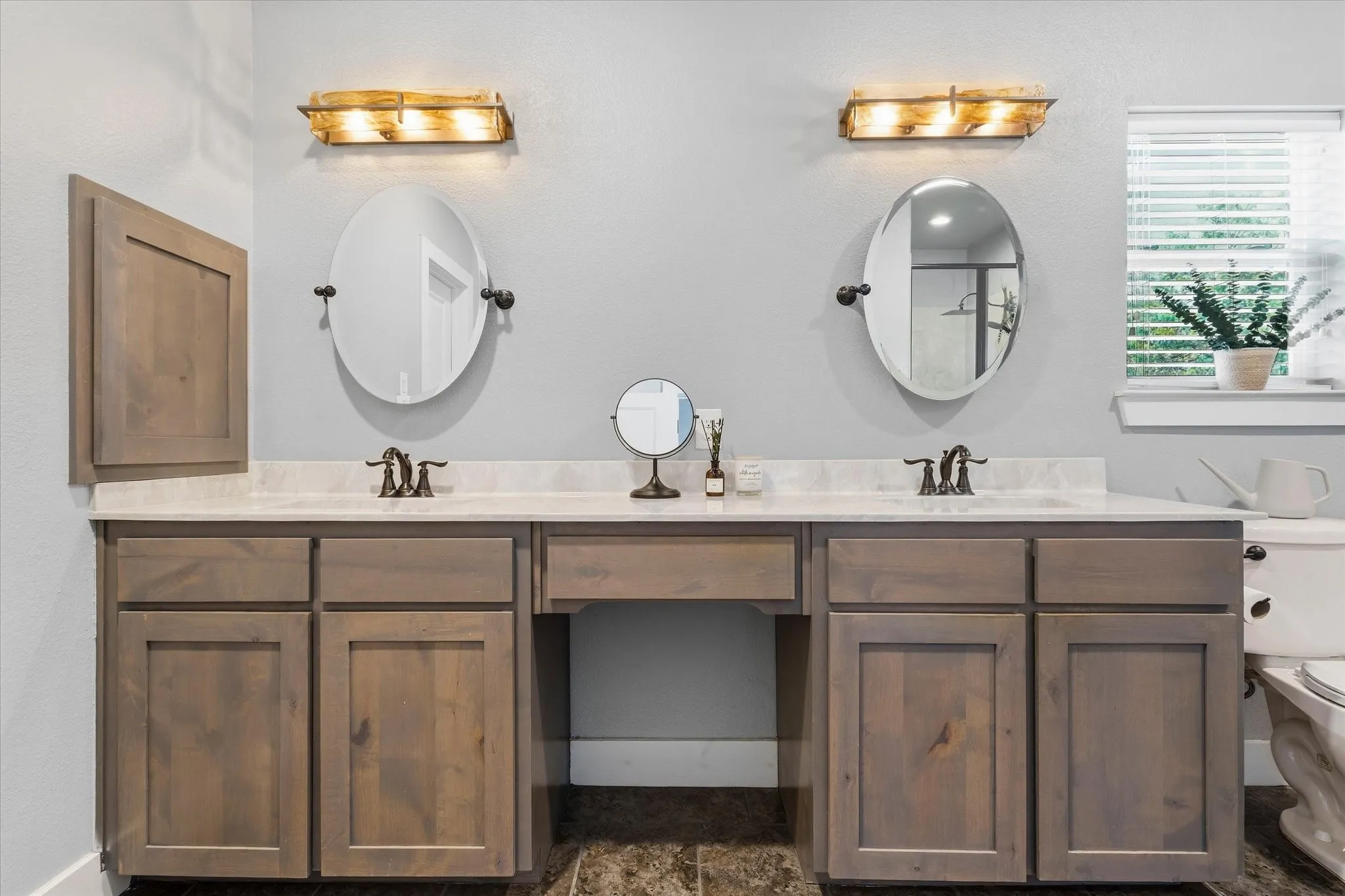 Dual vanity with light wood-finish cabinetry, integrated sinks, and individual wall-mounted lighting fixtures
